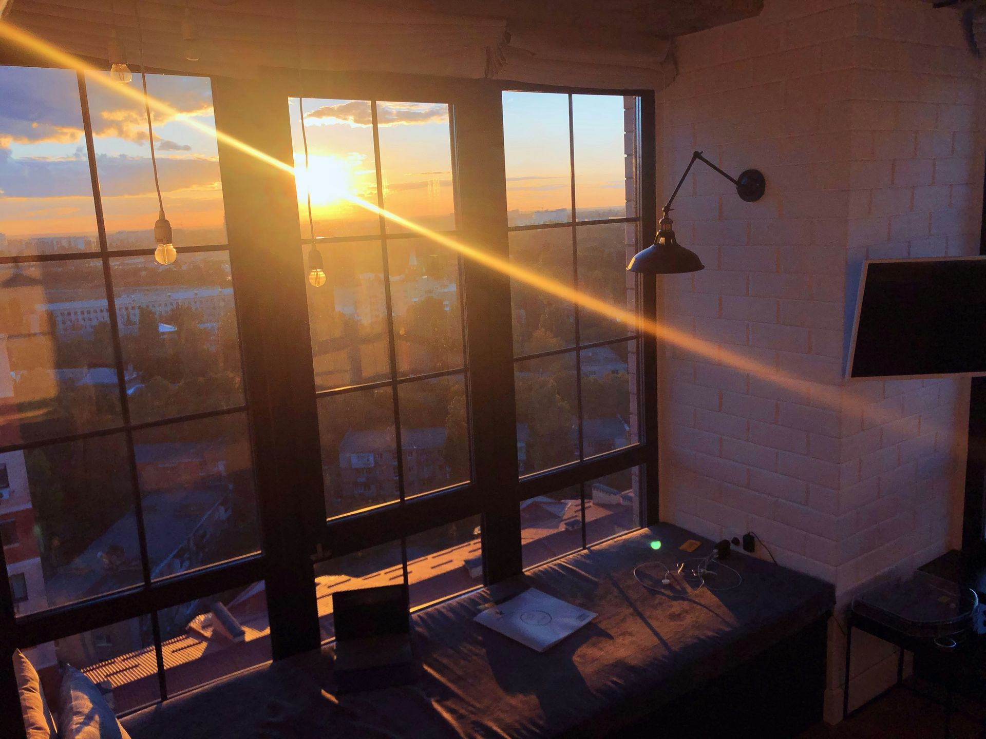 Sunset view through windows, illuminating a desk with laptop and lamp in a loft-style room.