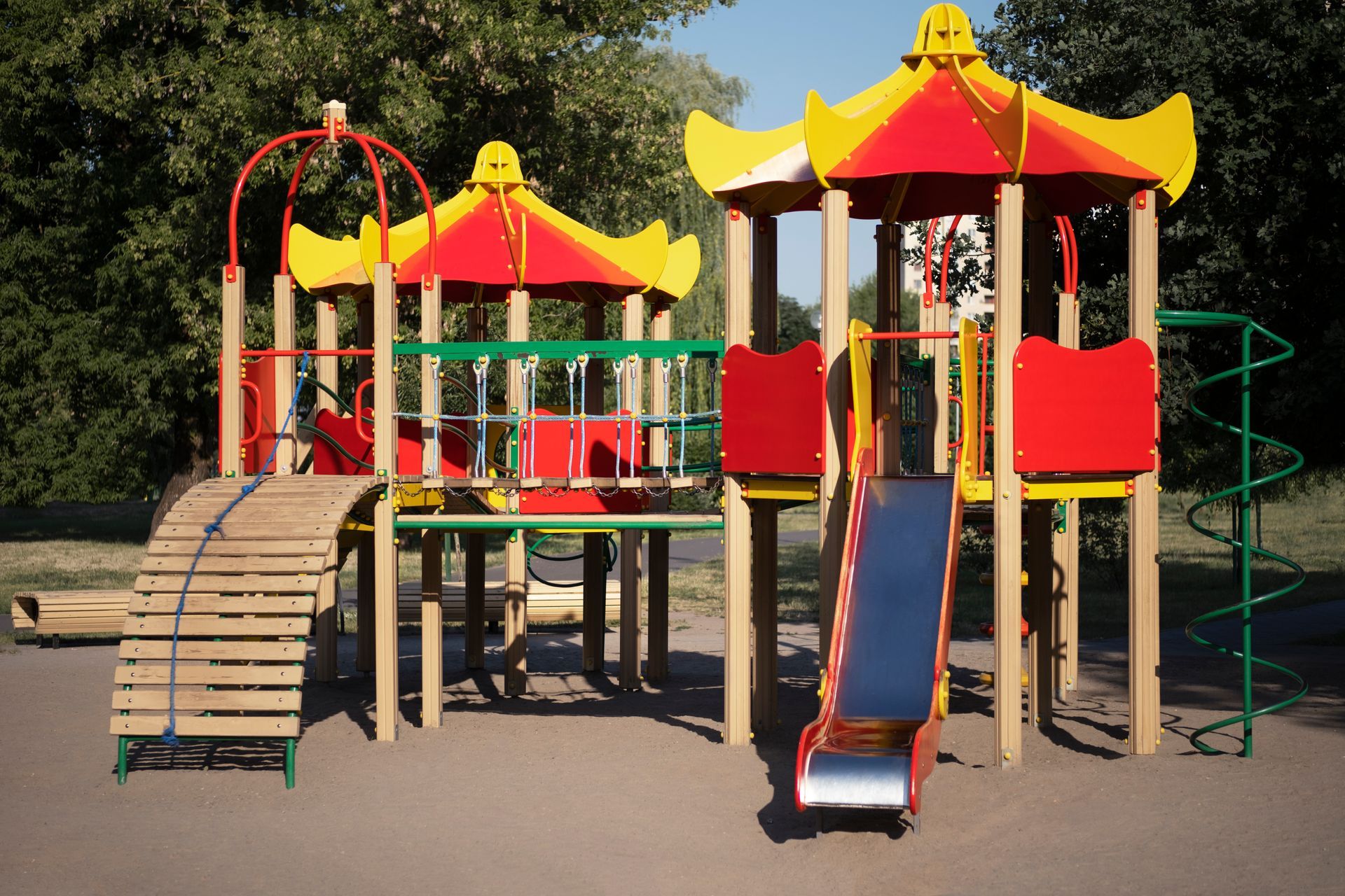 Playground with red, yellow, and green structures, featuring a slide, climbing ramp, and spiral slide.