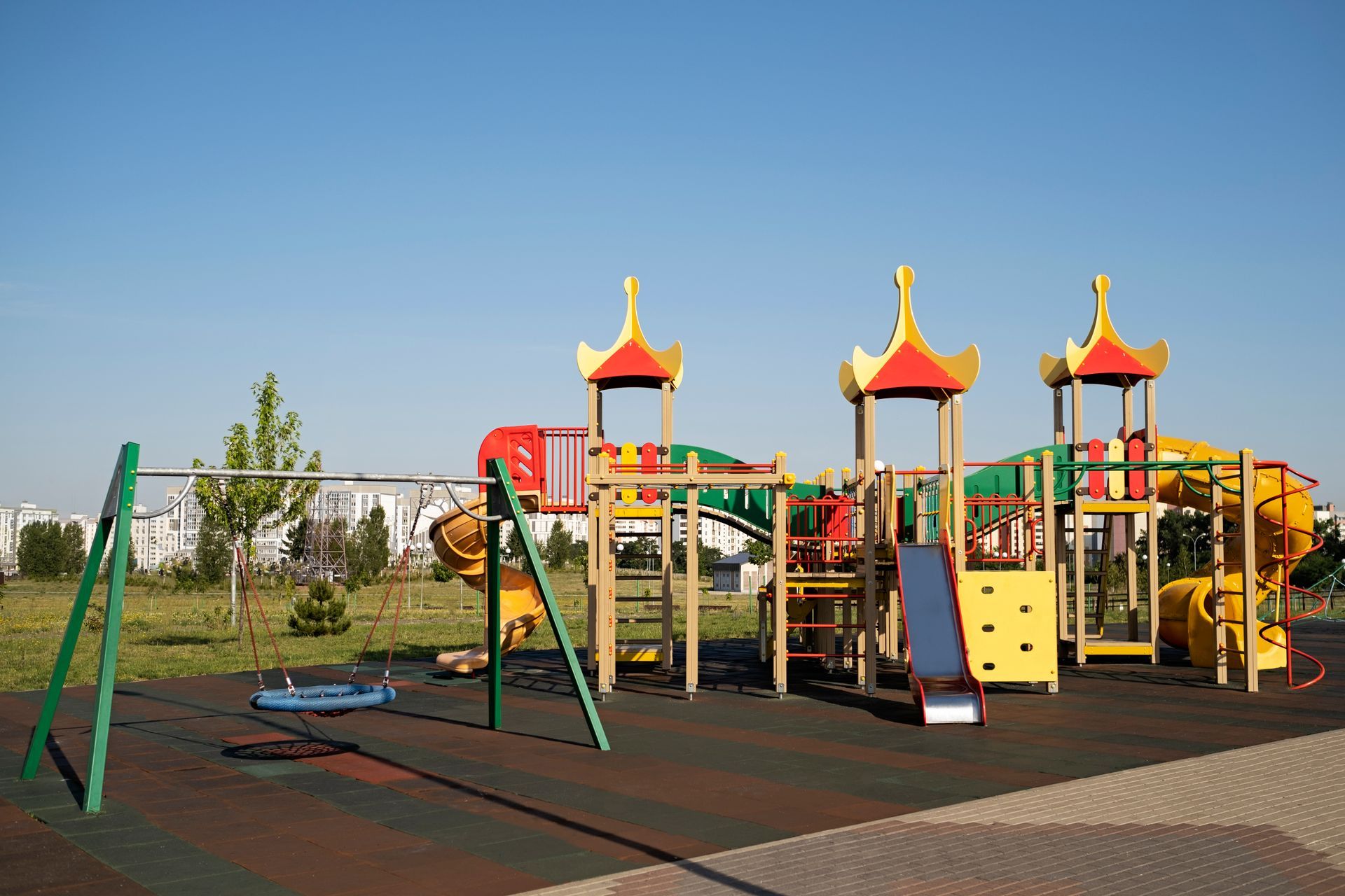 Playground with swings and colorful climbing structures on a rubber surface under a blue sky.