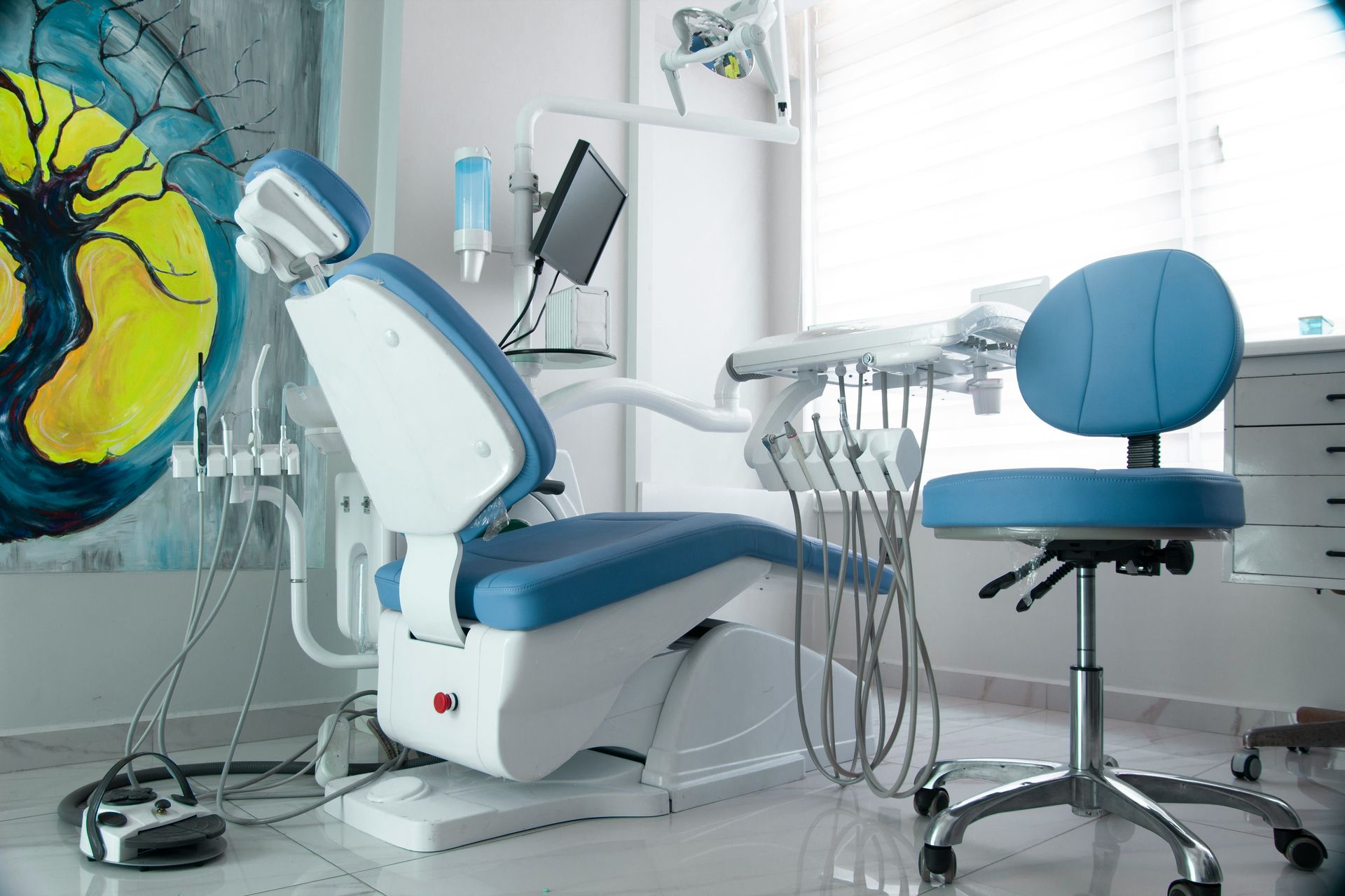 Dental examination room with blue and white chair, tools, and assistant's stool.