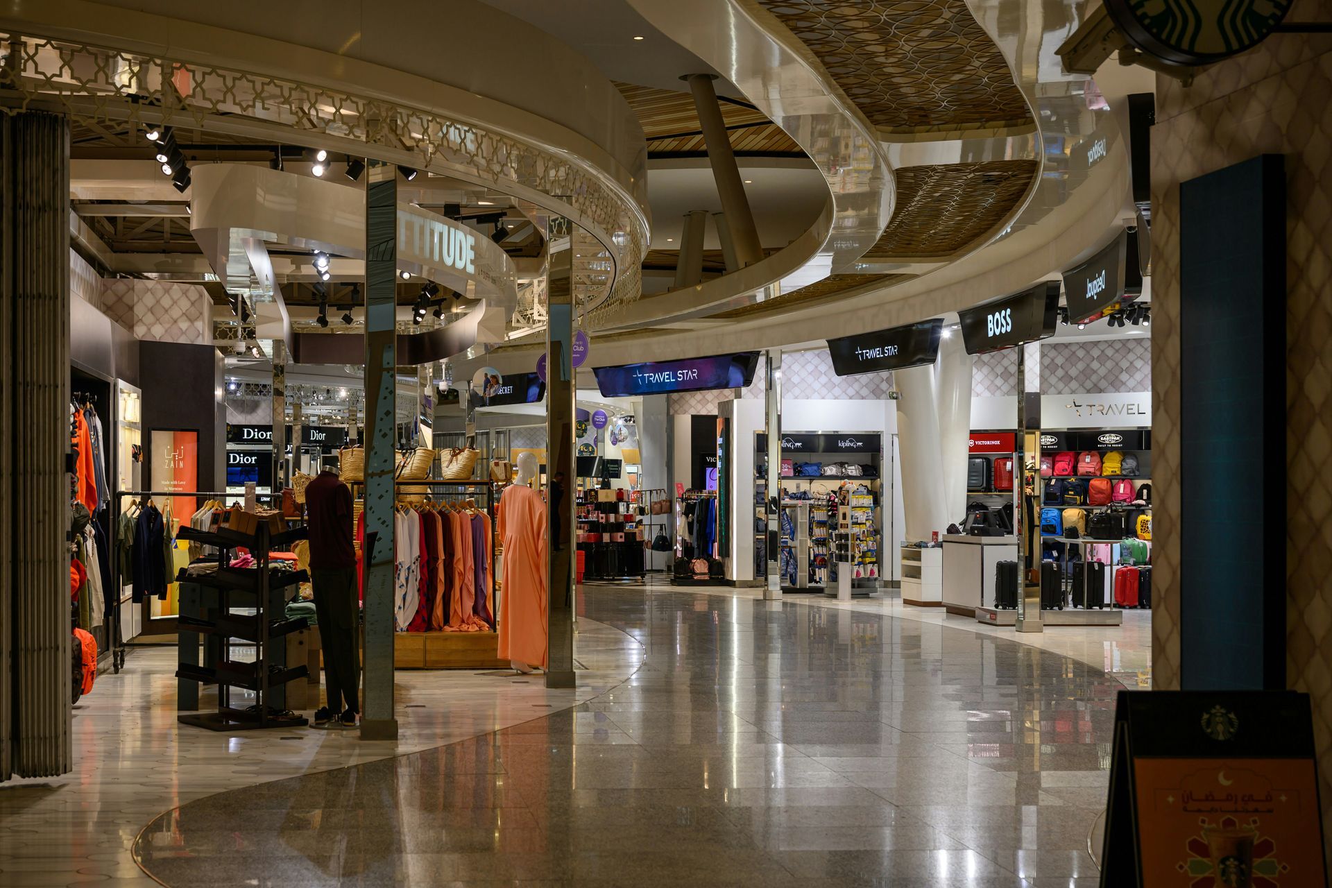 Interior view of a shopping mall hallway with retail stores, decorative ceiling, and a polished floor.