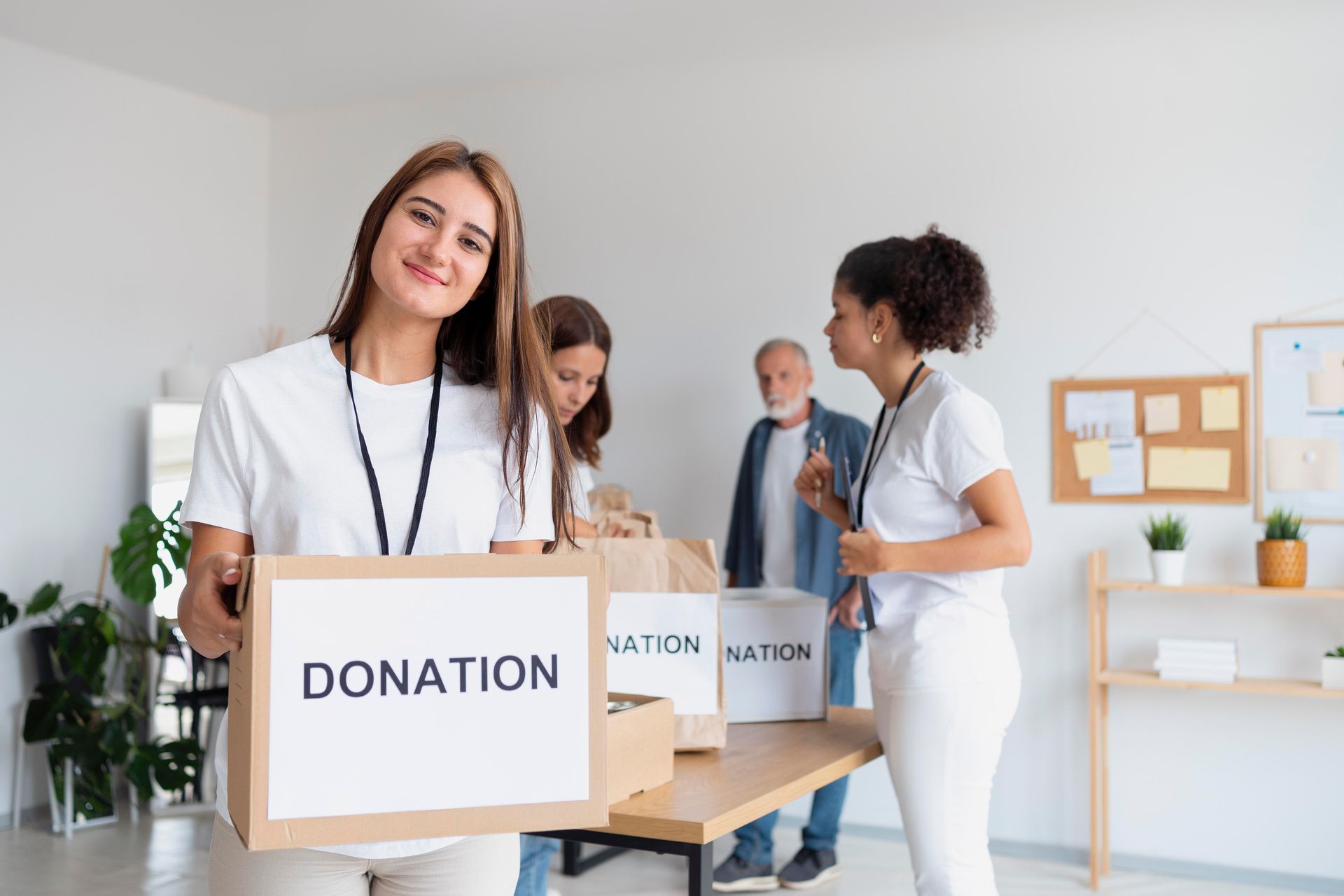 Volunteers packing donations in a light-filled room. Woman holds a box labeled 