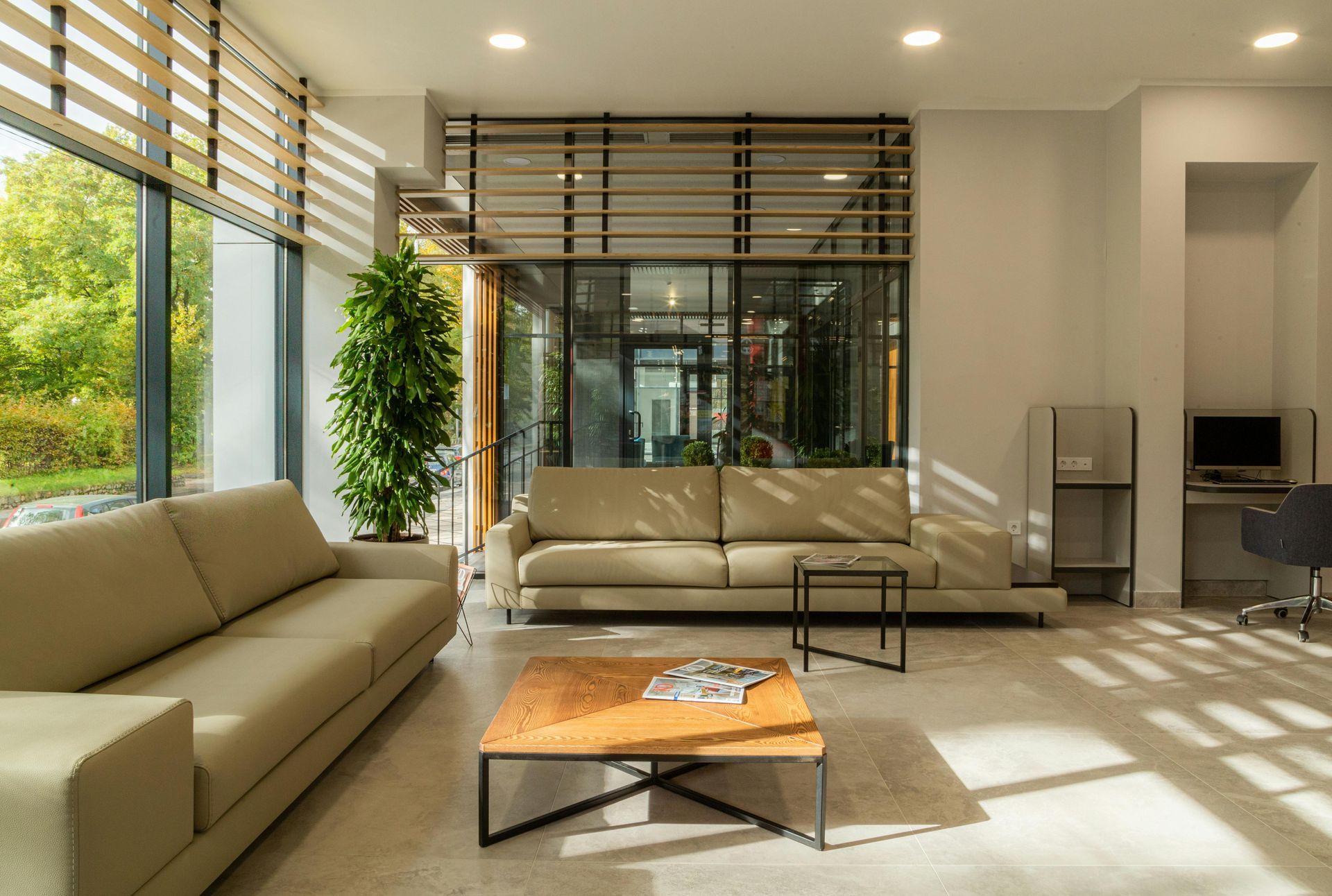 Modern living room with neutral-toned sofas, large windows, and a coffee table, flooded with sunlight.