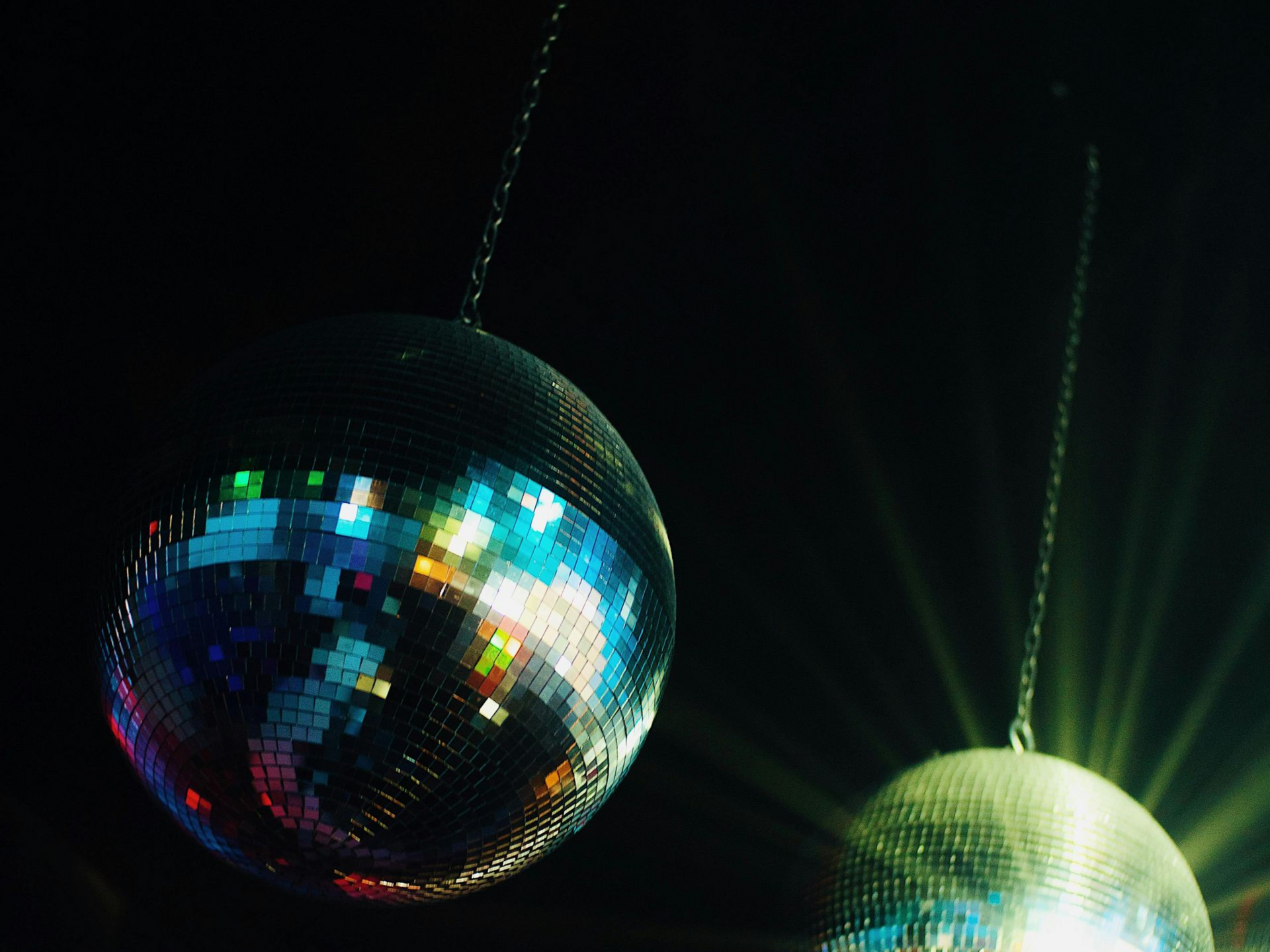 Two disco balls hanging against a dark background, reflecting colorful light.
