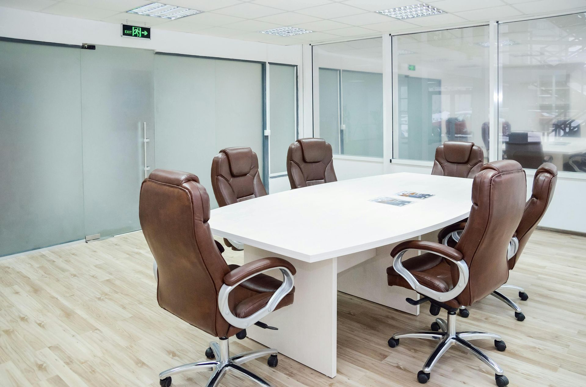 Conference room with a white table, brown leather chairs, and frosted glass door.