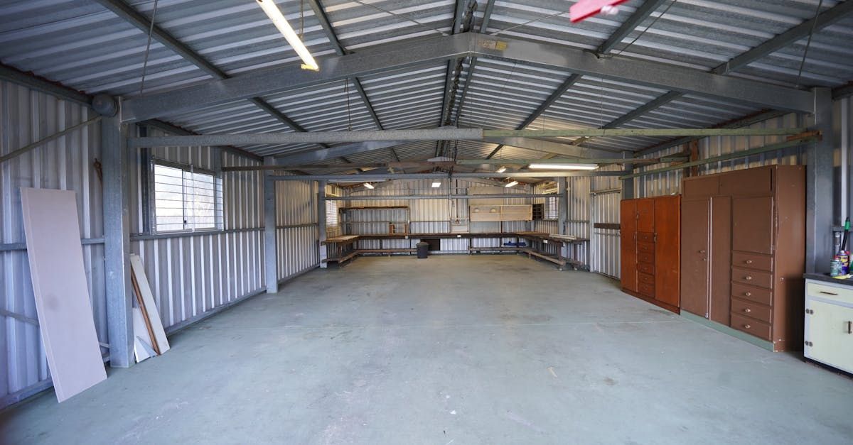 Empty metal-walled garage with concrete floor. Workbenches along back wall, cabinets on right.