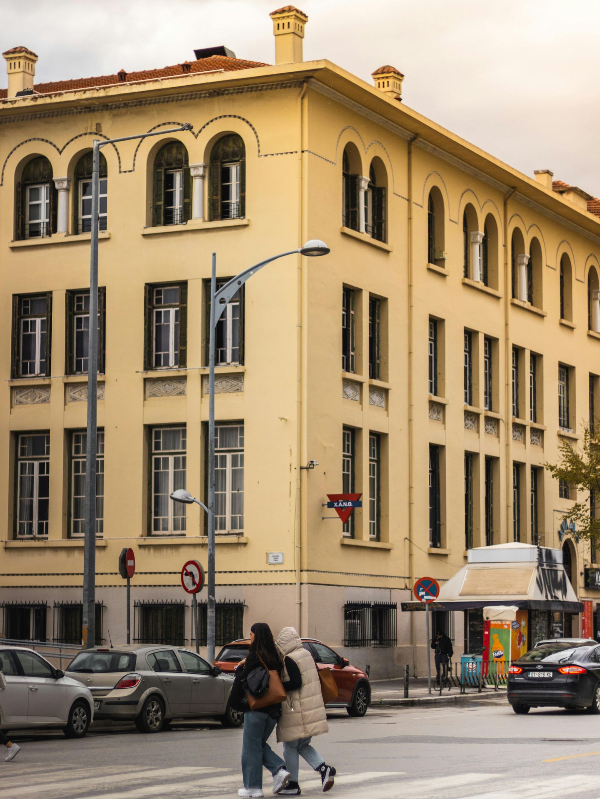 Yellow building at a street corner with pedestrians, cars, and streetlights.