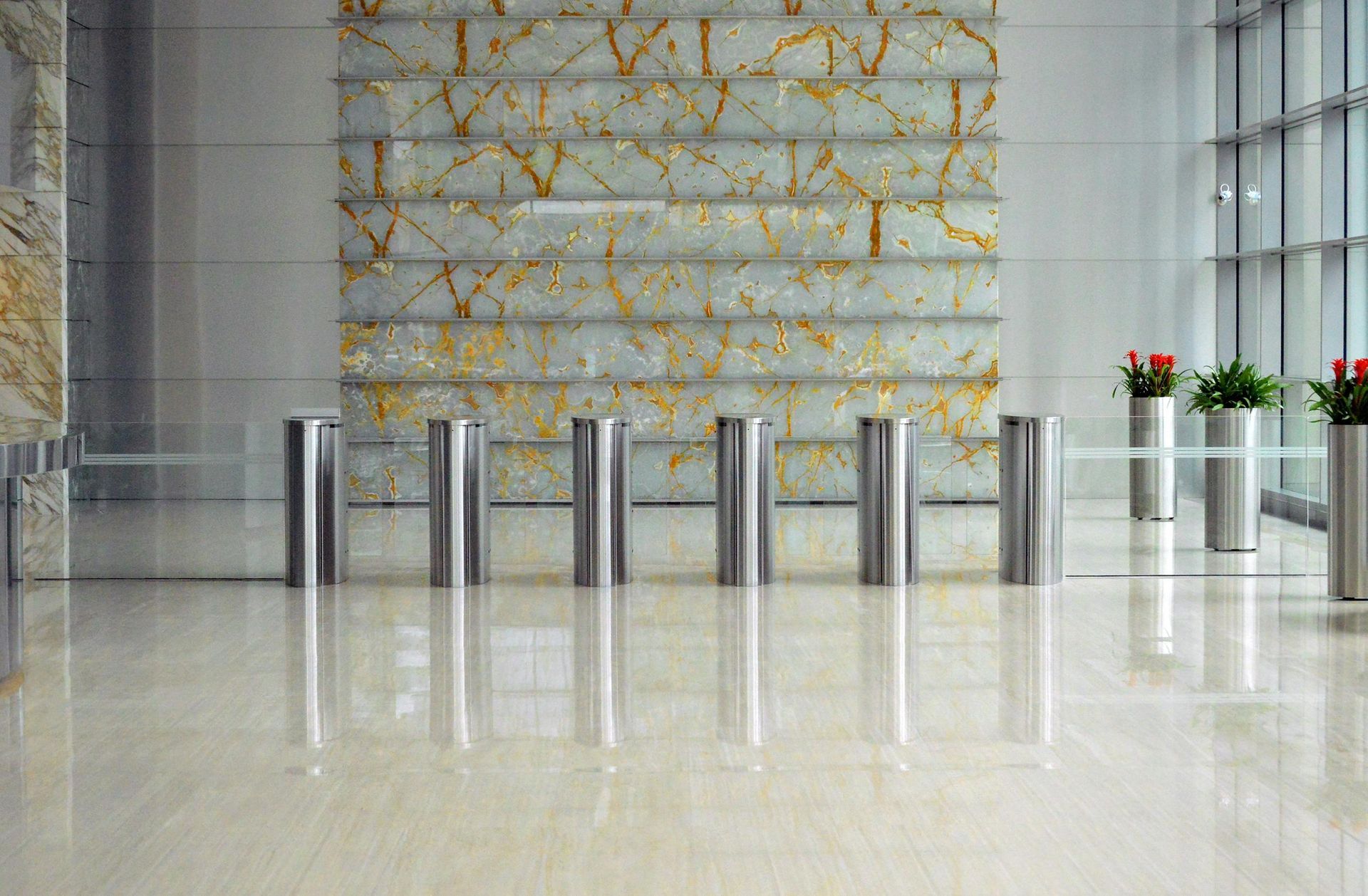 Stainless steel turnstiles in a modern lobby with marble flooring and decorative wall panel.