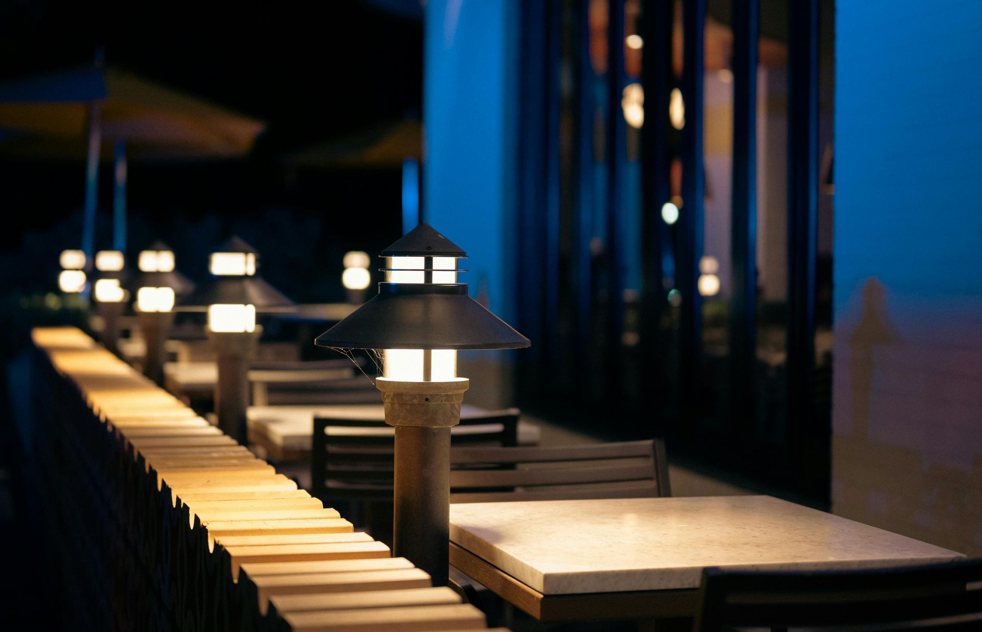 Outdoor restaurant seating at night, lit by decorative lamps, with tables and chairs.