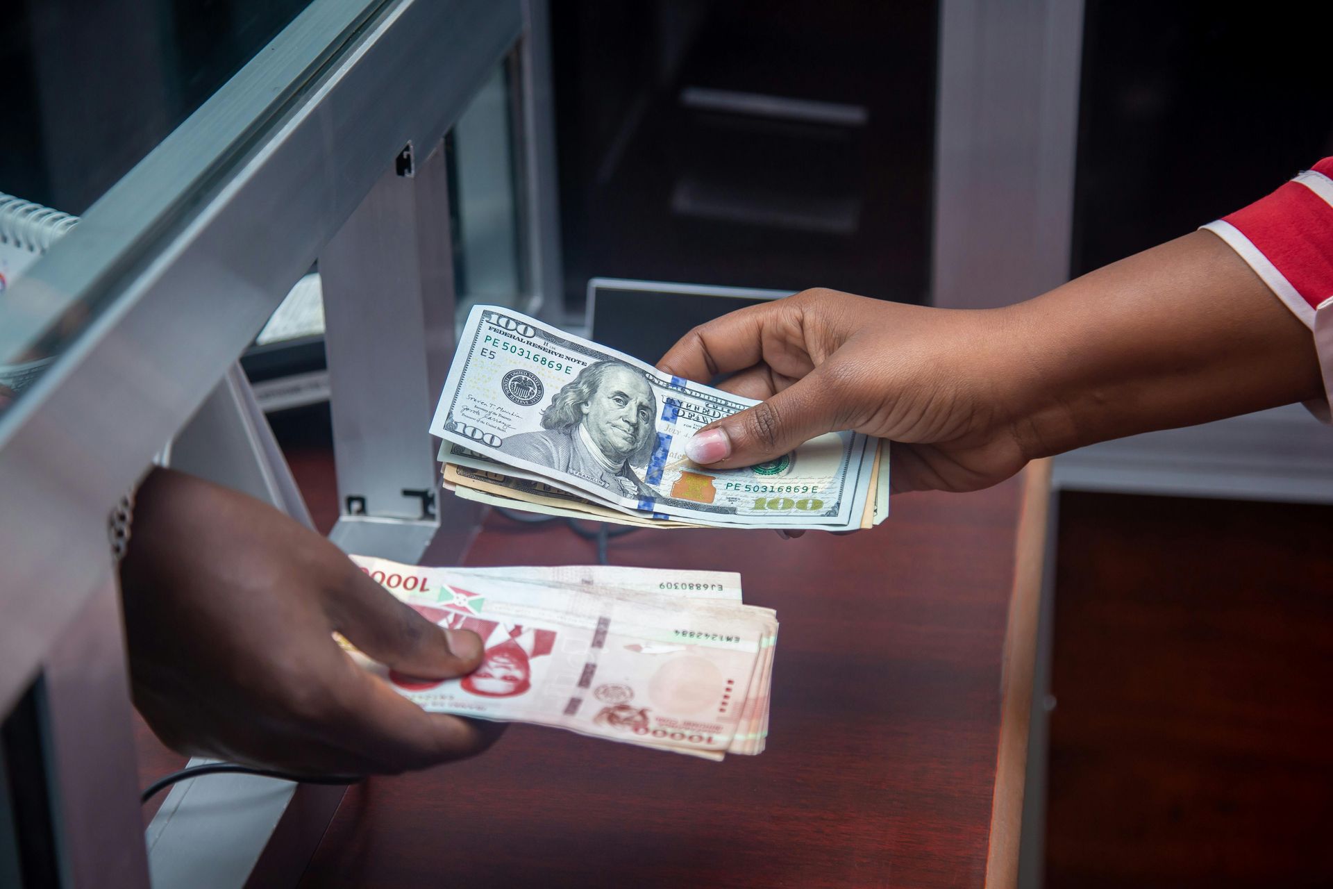 Hands exchanging US dollars and another currency at a bank counter.