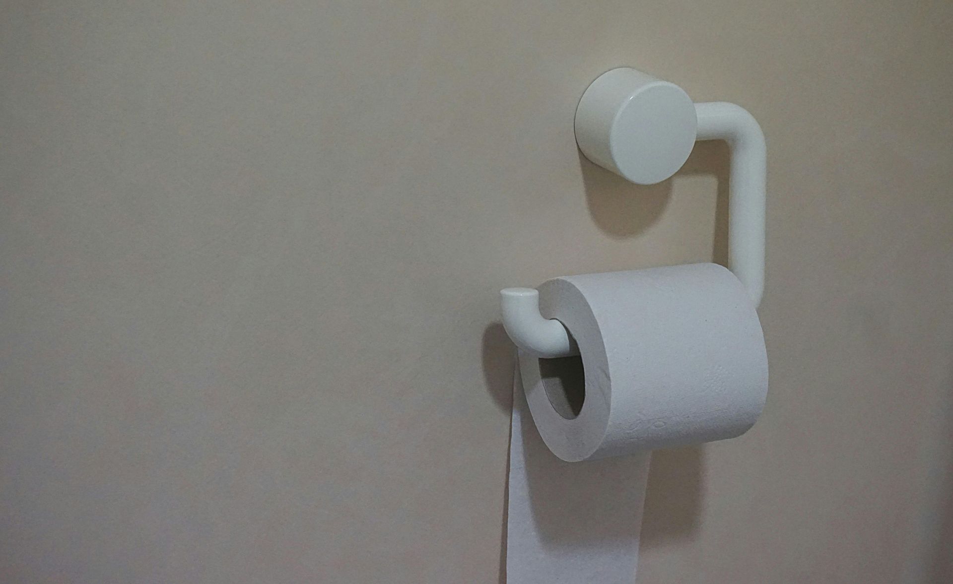 White toilet paper roll on a white holder attached to a beige wall.