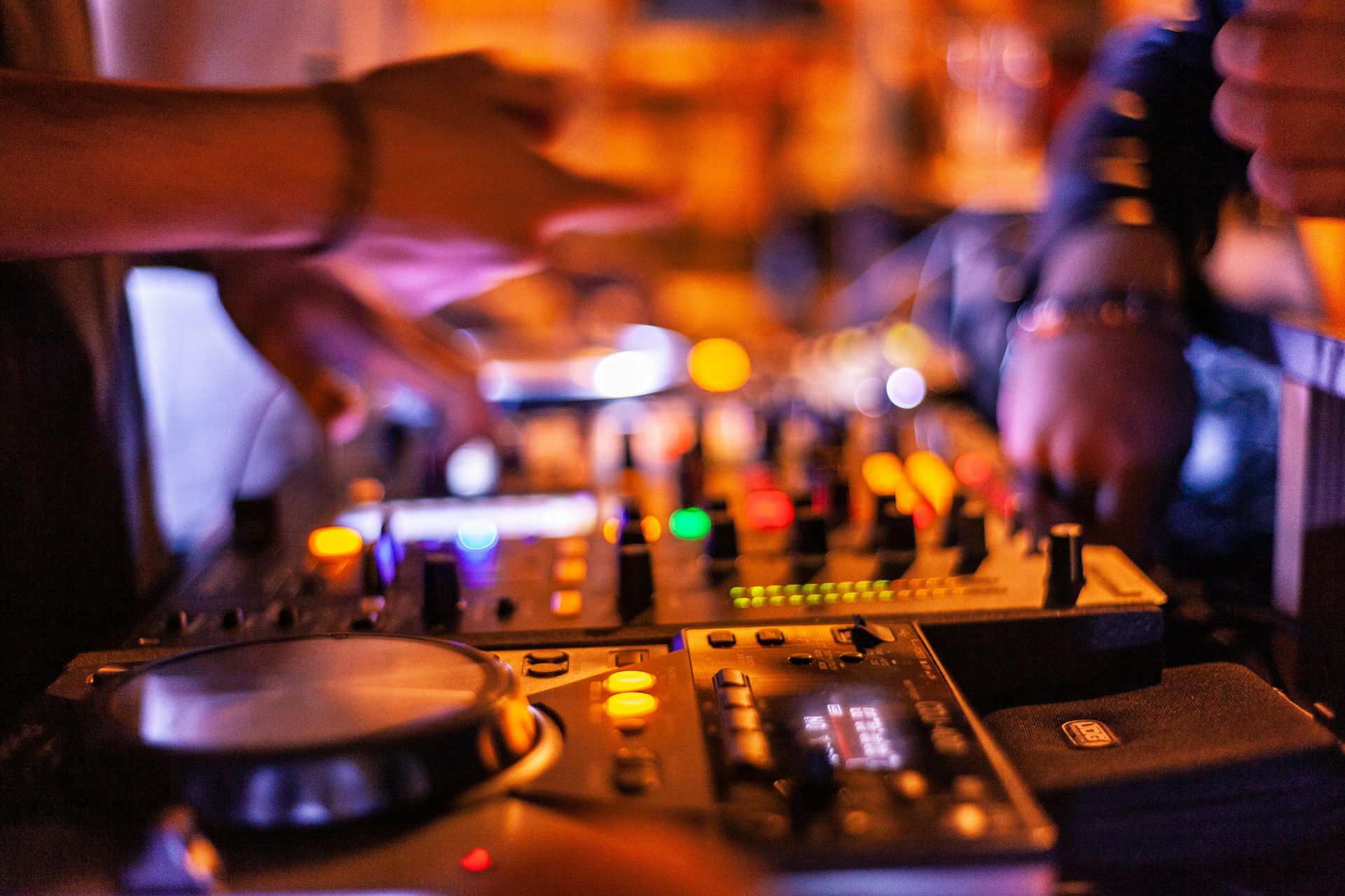 DJ at work, hands on a mixing console with lights, in a dim, energetic setting.
