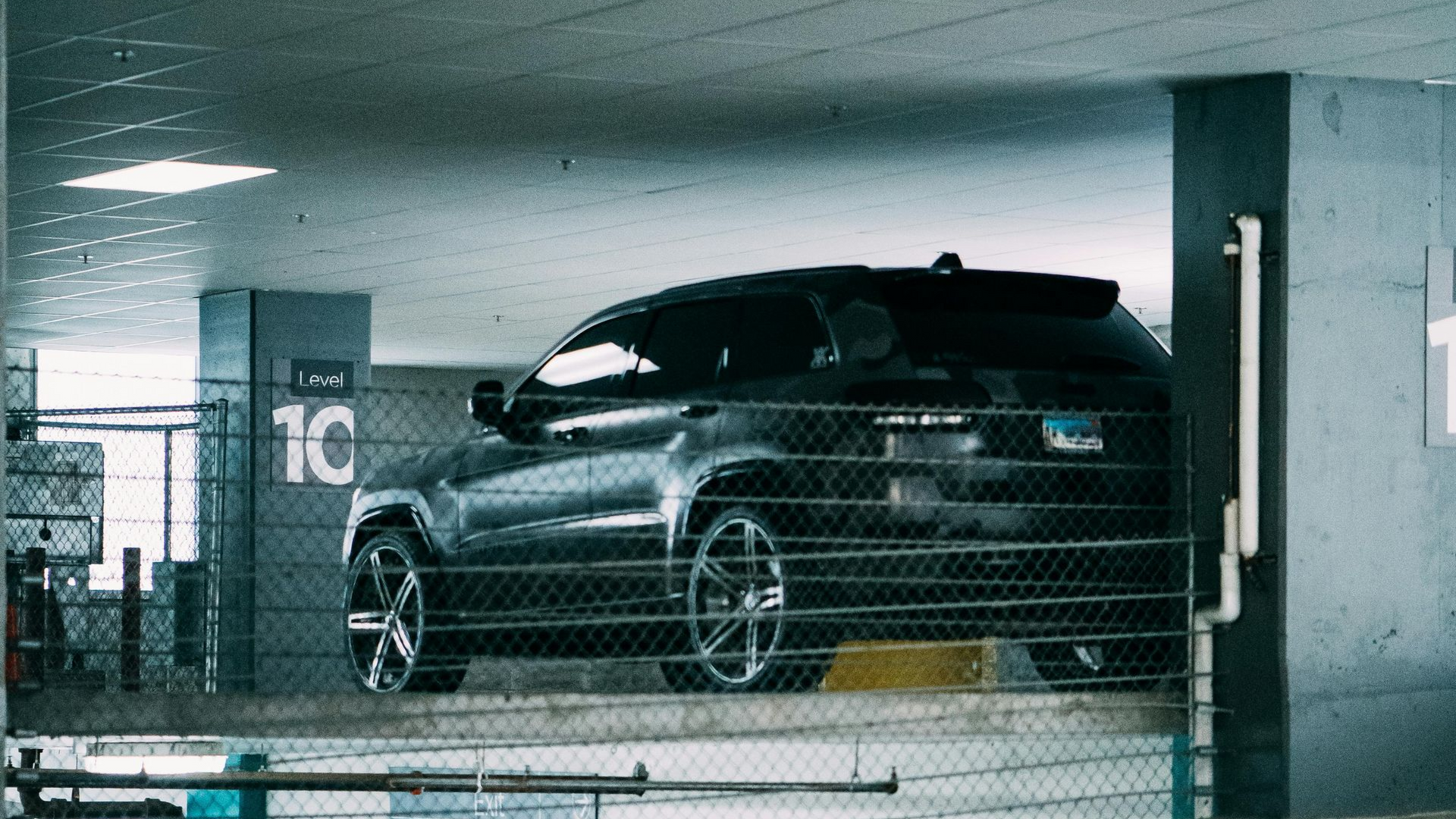Black SUV in a parking garage; partially obscured by a metal fence.