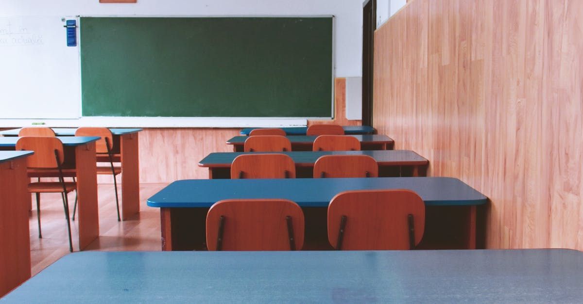Empty classroom with blue desks, orange chairs, green chalkboard, and wooden walls.