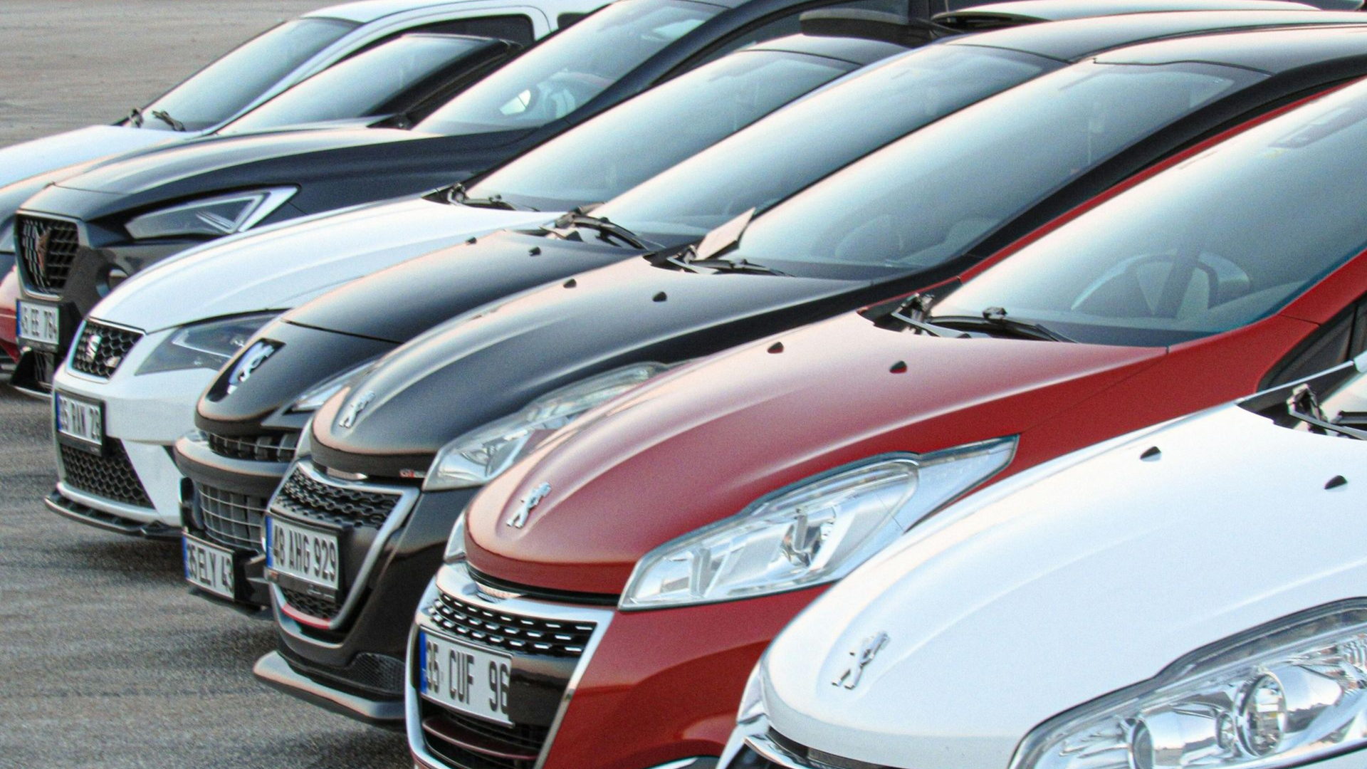 Cars parked in a row, various colors including red, white, black, and gray, outdoors.