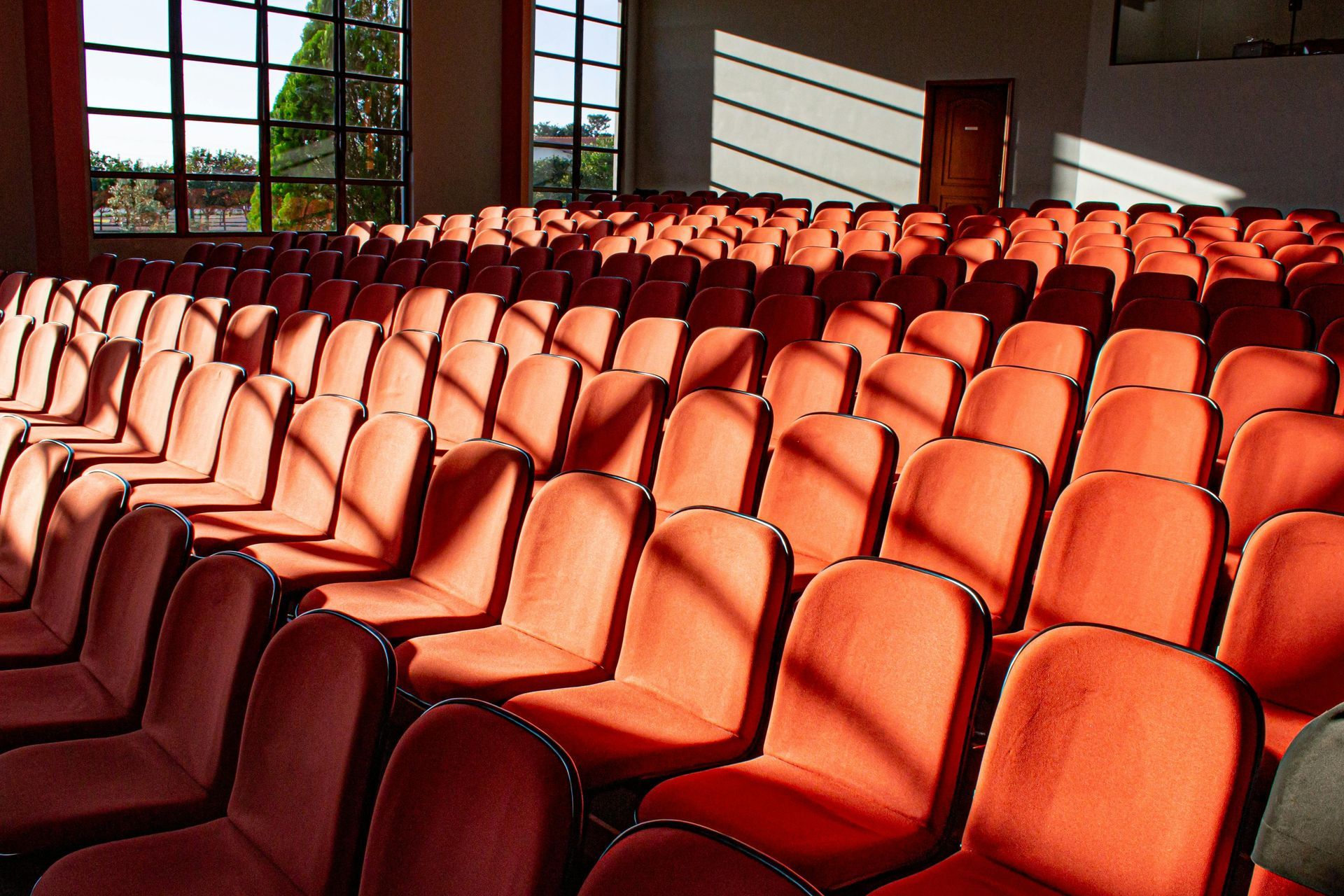 Rows of empty orange theater seats, with sunlight streaming through windows.