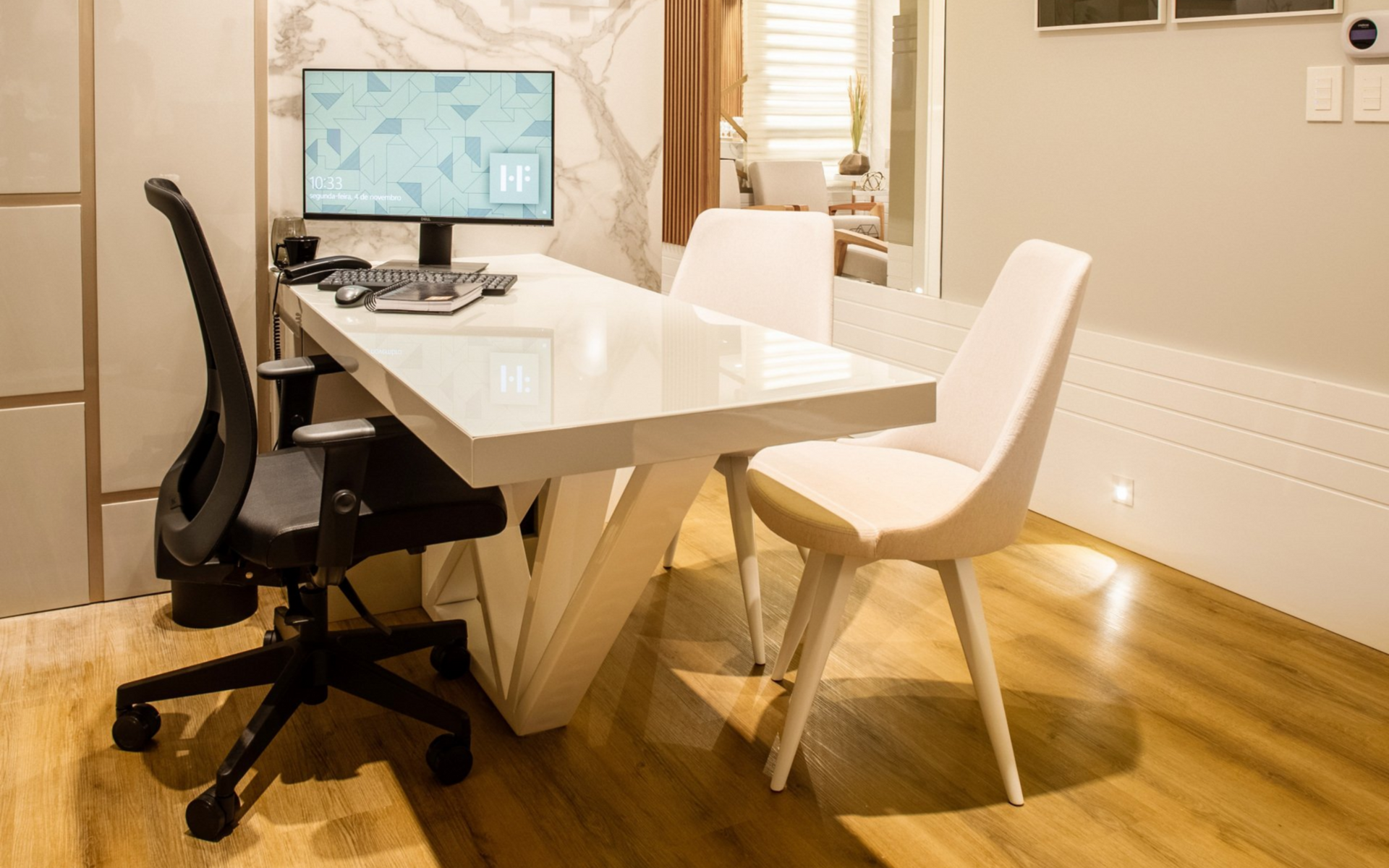 Office desk with computer, black office chair, two white chairs. White desk with marble and wood accents.