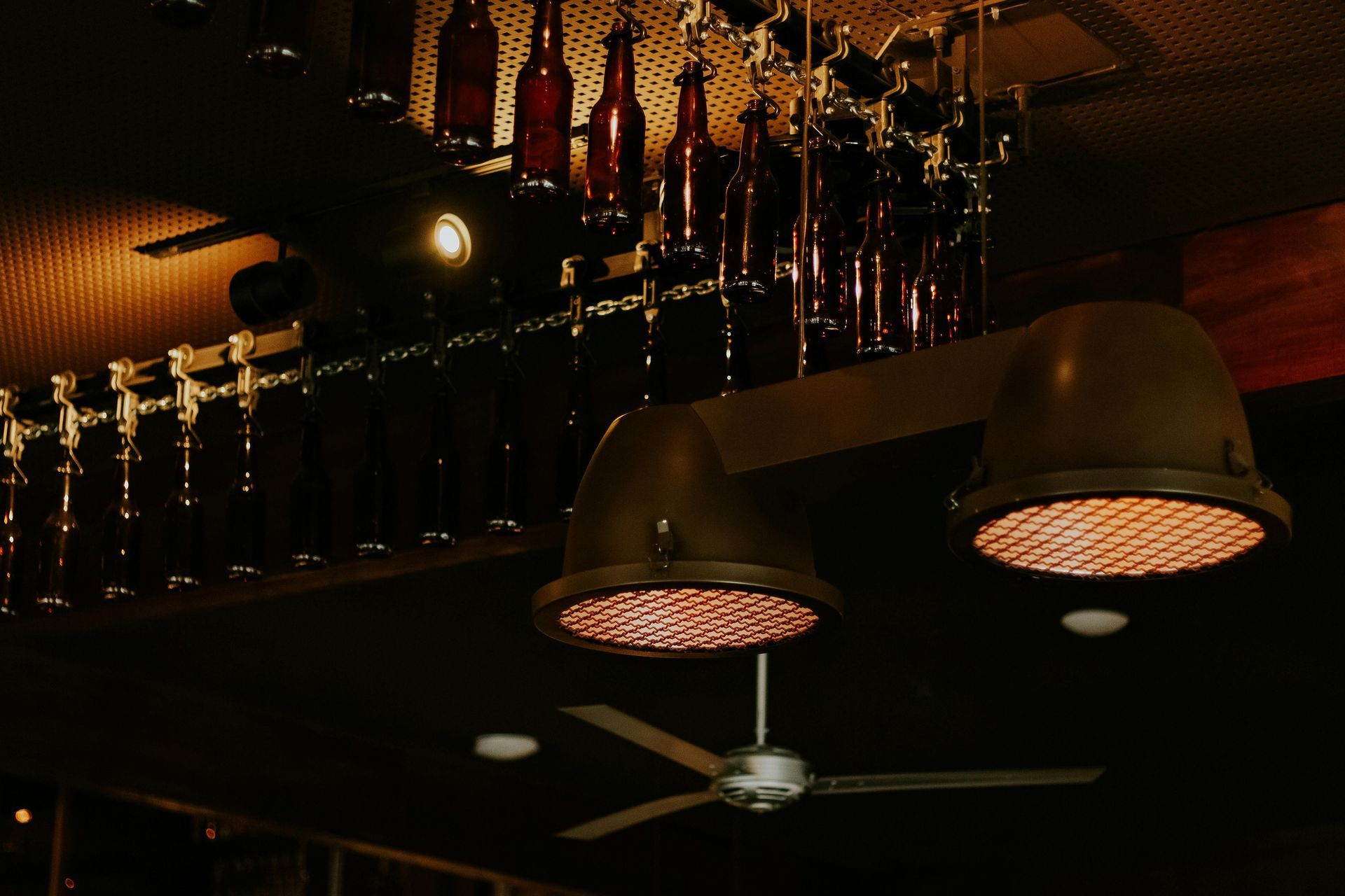 Industrial-style ceiling with a large light fixture, decorative bottles, and a ceiling fan.