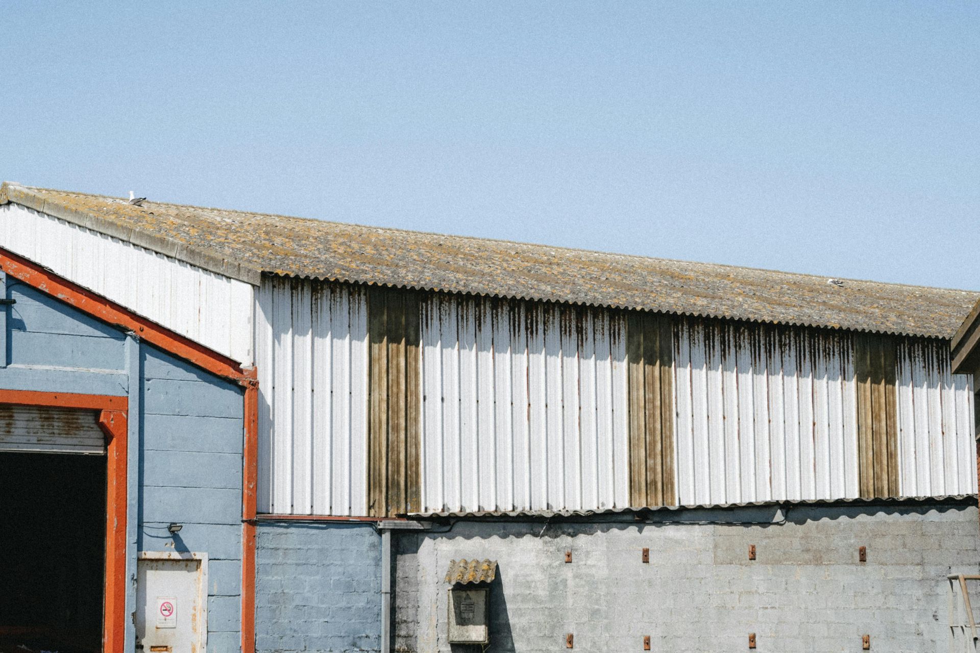 Barn with corrugated roof, white siding, and blue wall under a clear sky.