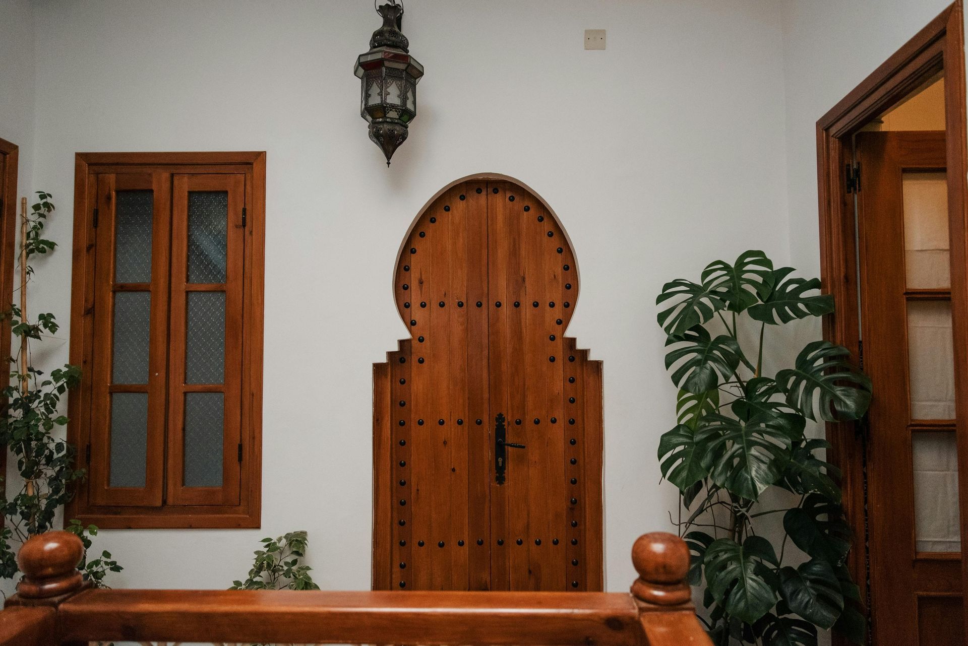 Wooden arched doorway with a hanging lamp, window, and greenery against a white wall.