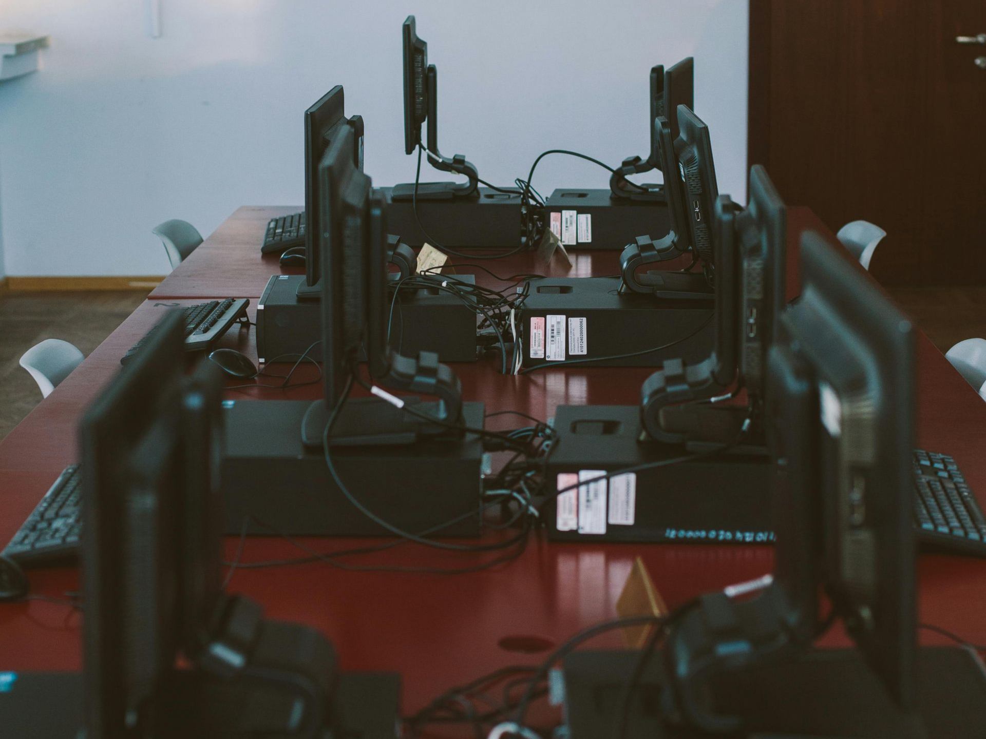 Computer lab with multiple computer monitors, keyboards, and processors on a long, red table.