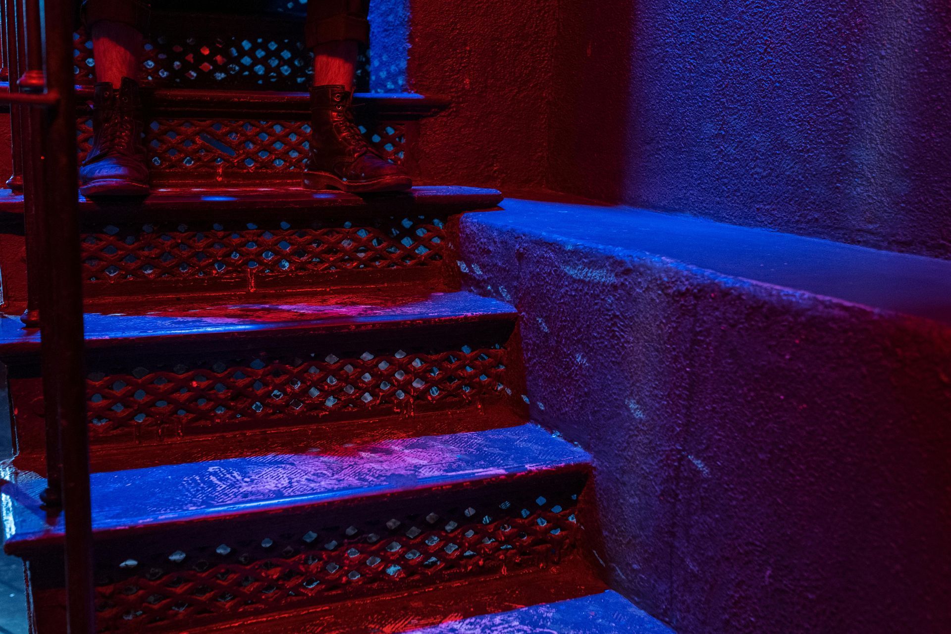Red and blue-lit metal spiral staircase in a dimly lit building corner.