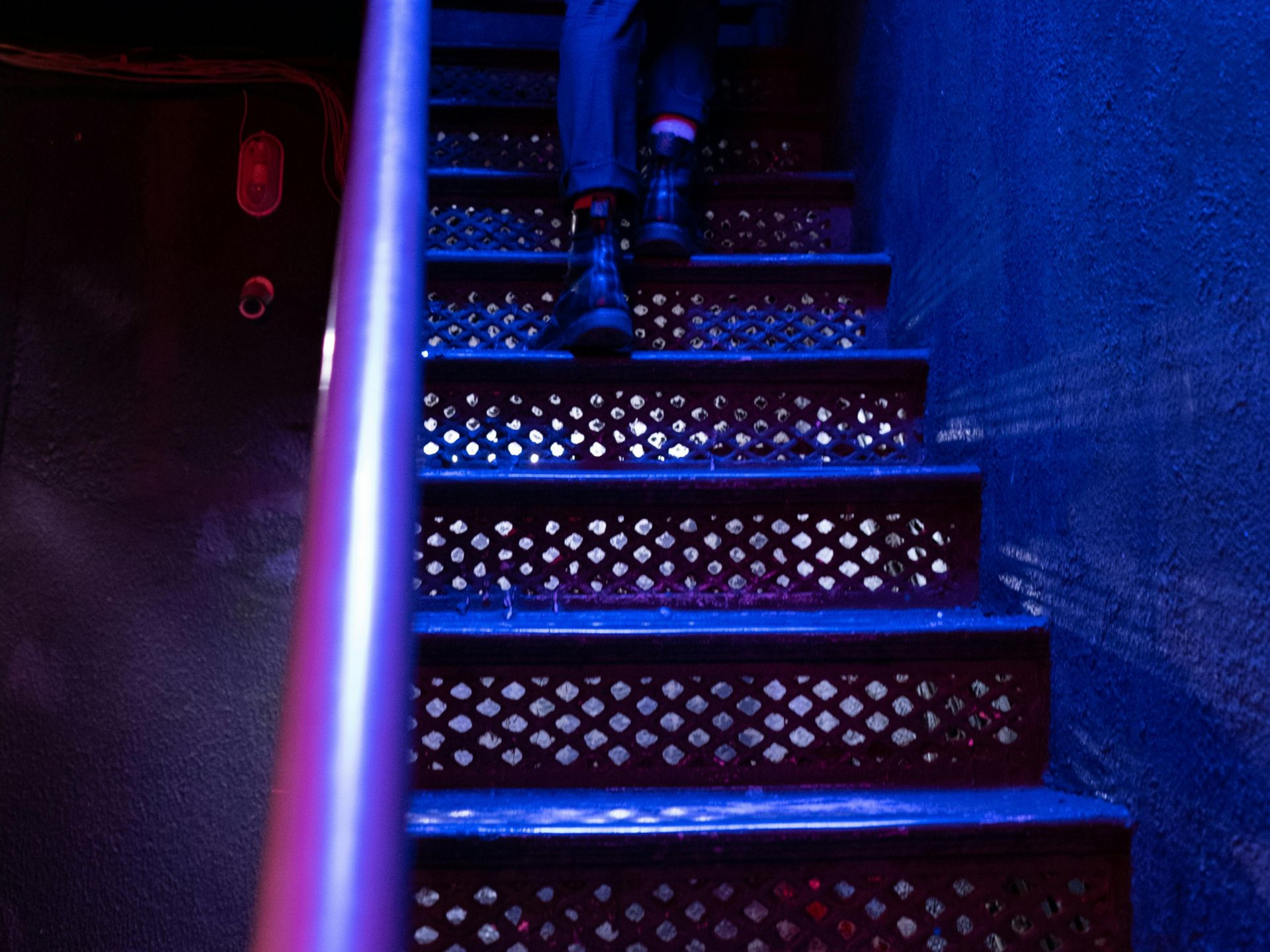 Person walking down metal stairs, illuminated by blue and red light.