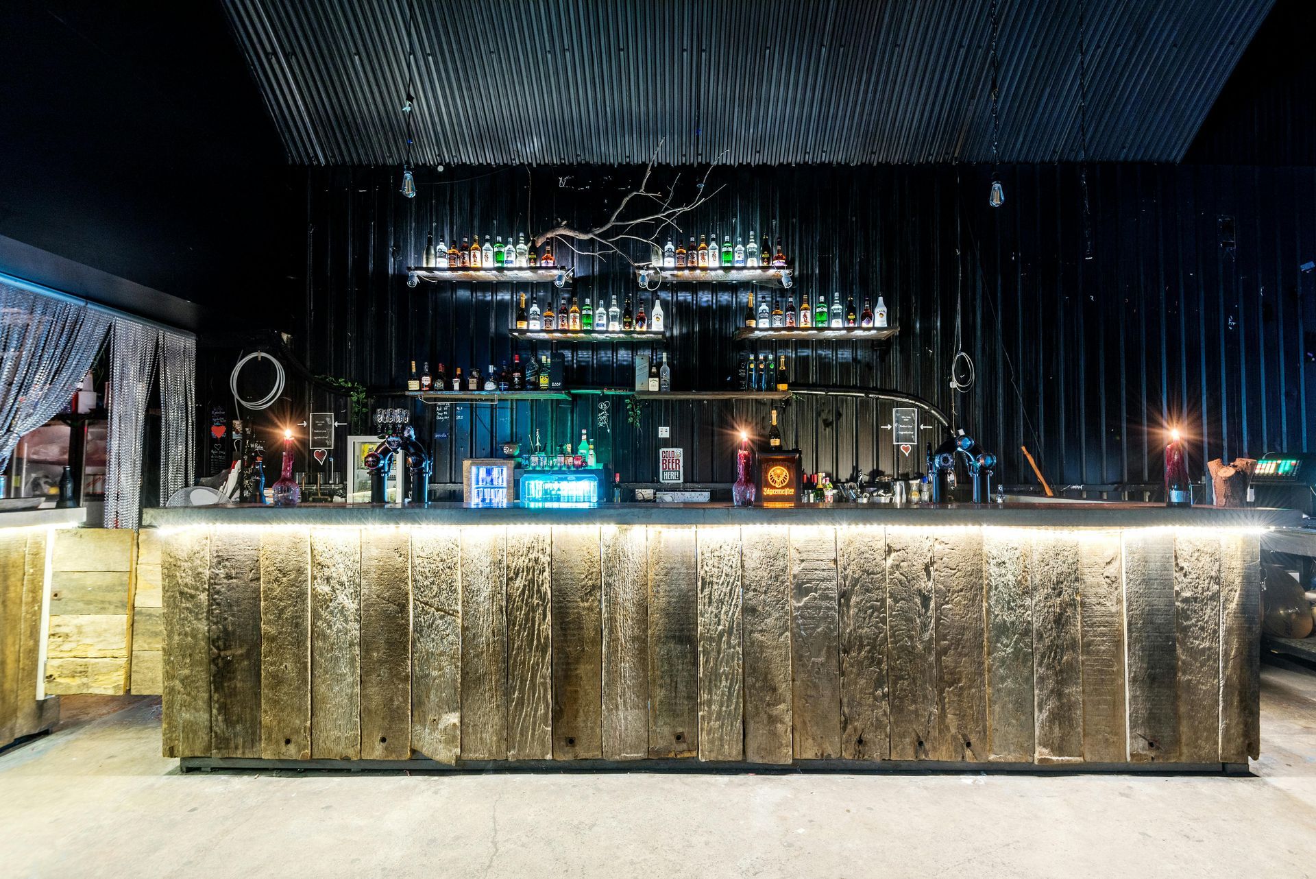 Bar with a weathered wood facade and lit countertop, bottles on shelves, dark interior.