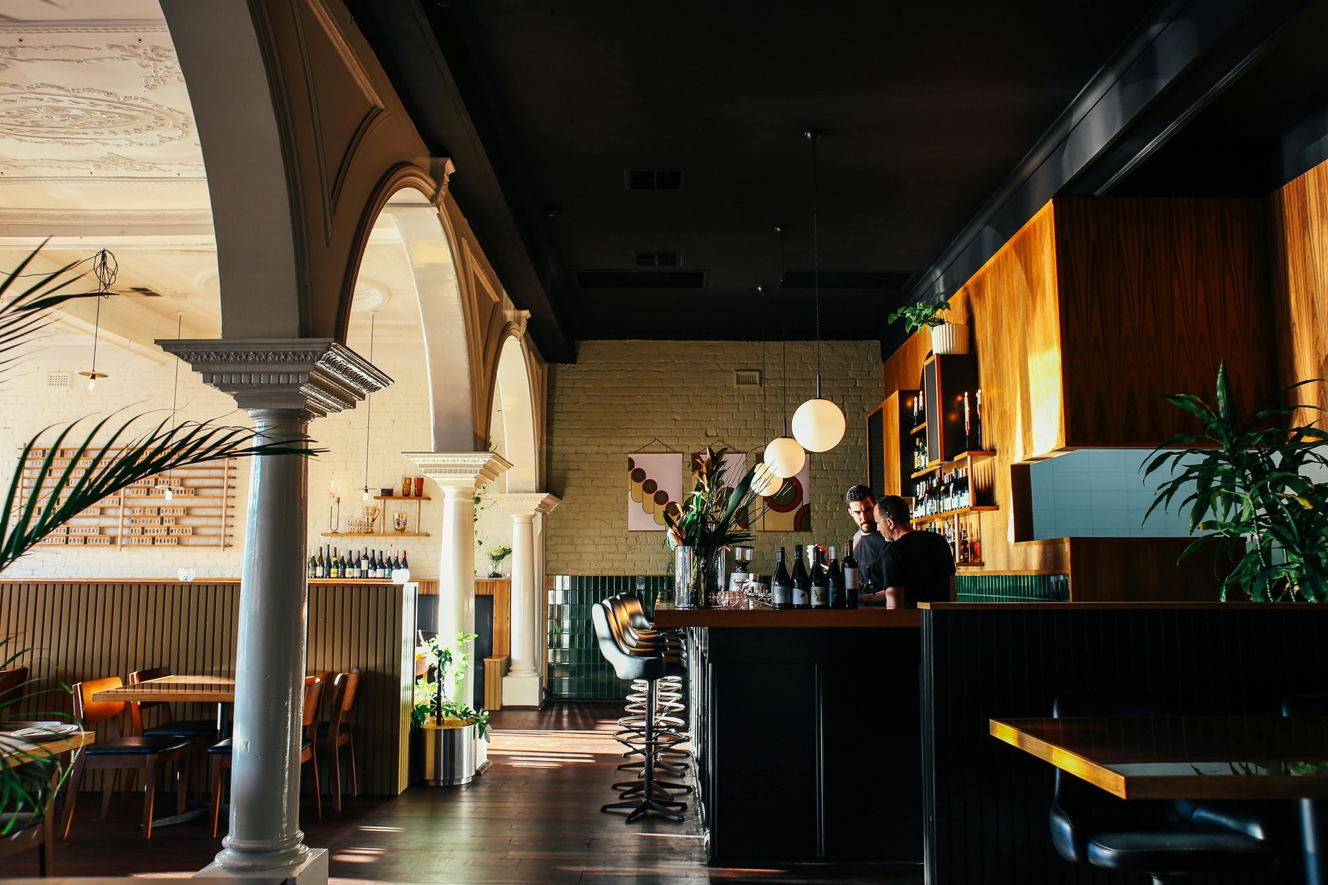 Restaurant interior with bar, arched columns, dark ceiling, wood paneling, and two people behind the bar.