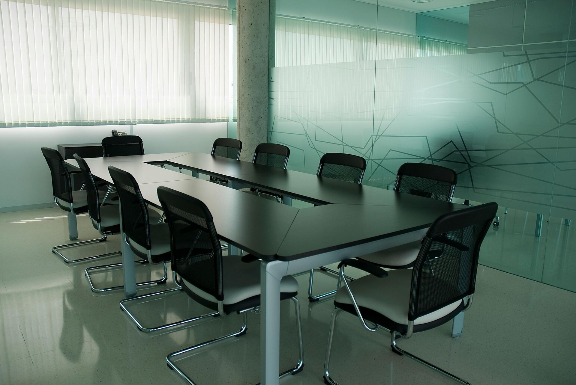 Conference room with a large table, chairs, frosted glass walls, and blinds.