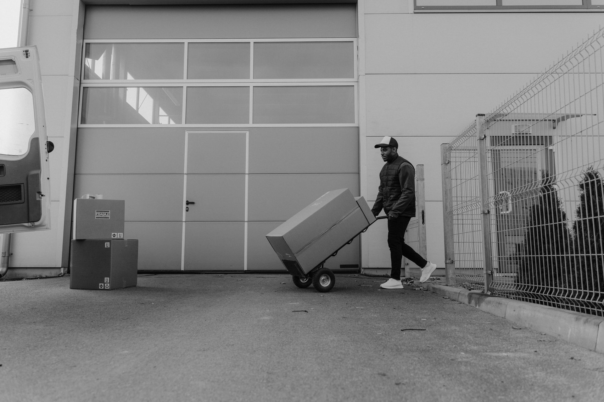 Person pulling a large box on a dolly outside a warehouse. Boxes are stacked nearby.