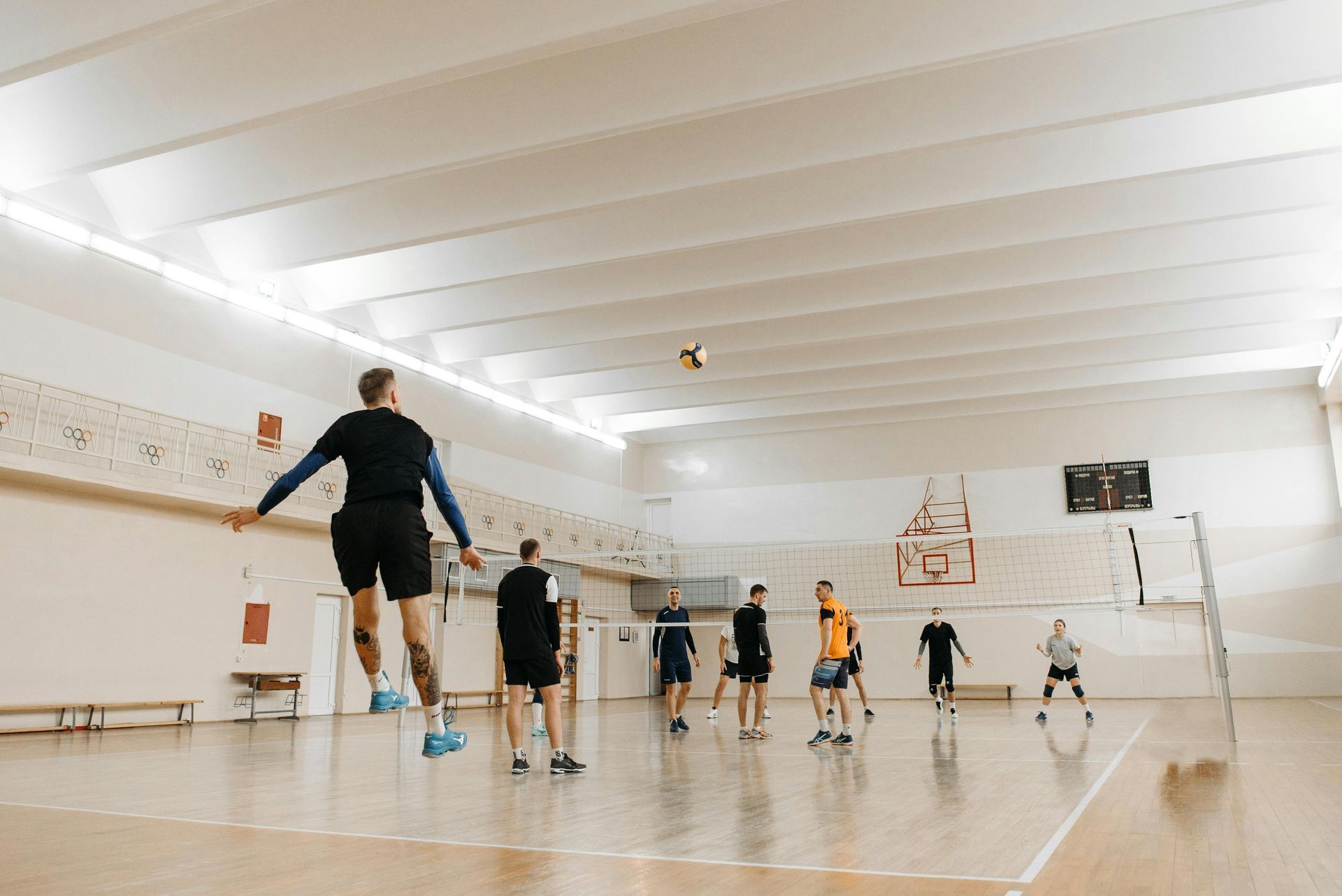 Volleyball player jumping to spike ball in a gymnasium, other players nearby.
