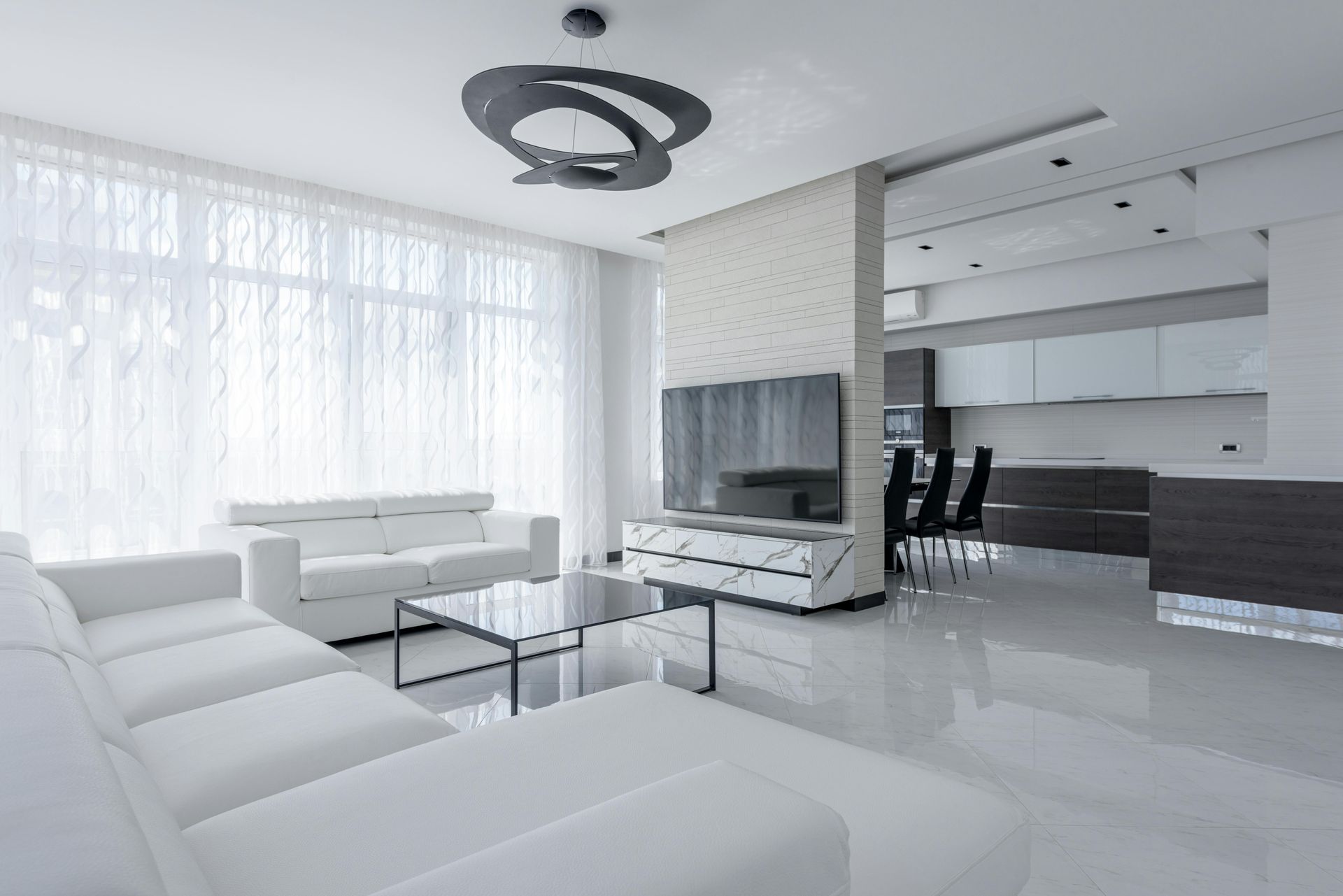 Modern white living room with couch, TV, and kitchen in the background.