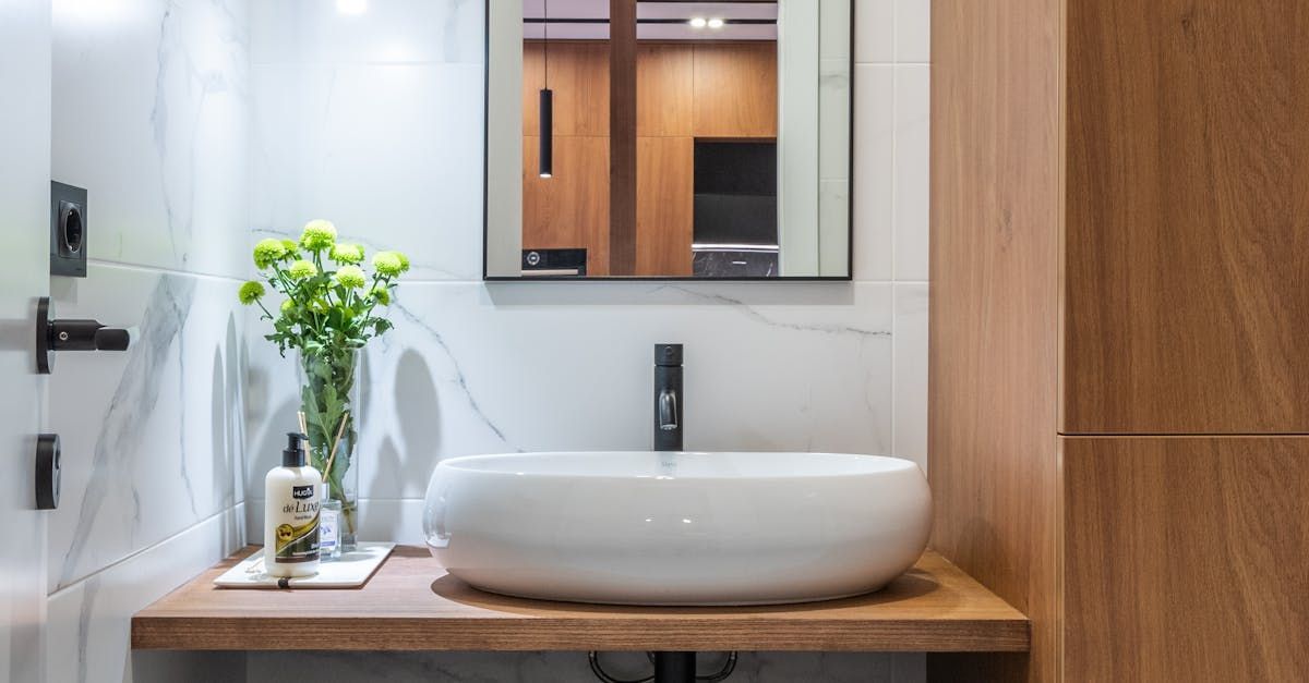 Modern bathroom with white vessel sink on wooden countertop, green flowers, black faucet, and wood paneling.