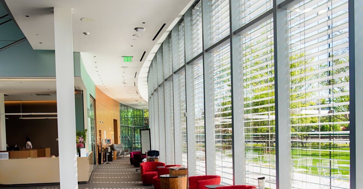 Modern interior with curved glass wall, red chairs, and trees visible outside.