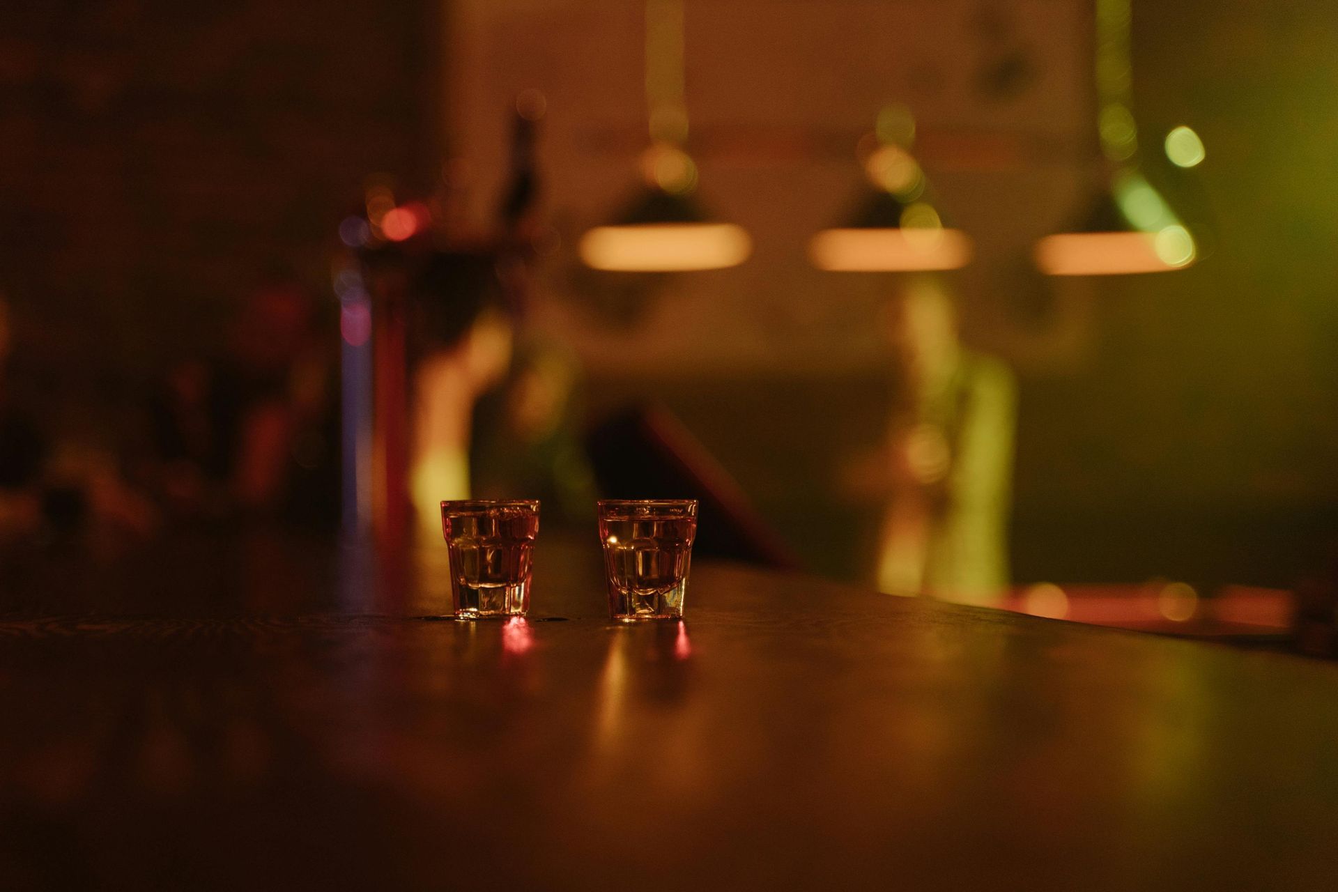 Two shot glasses on a bar. Warm lighting, blurred background of a bar scene.