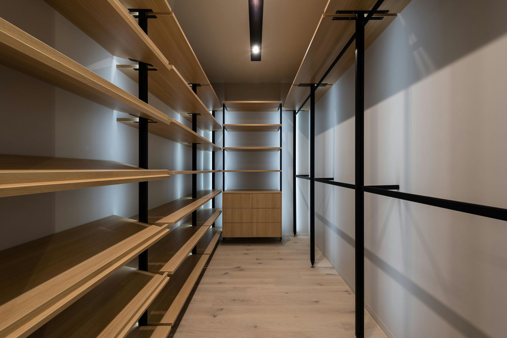 Walk-in closet with light wood shelves, black metal supports, and a central cabinet.