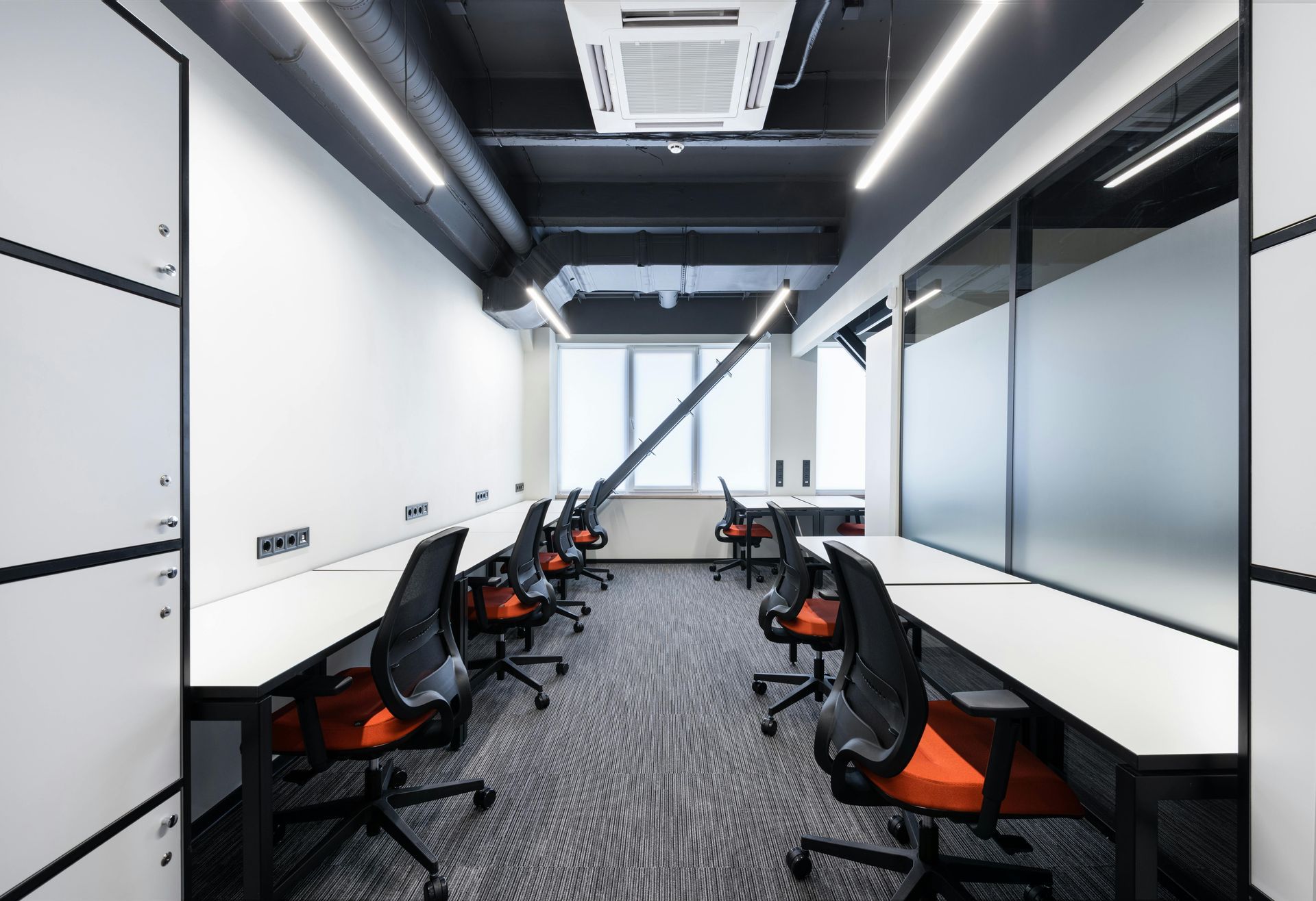 Modern office space with desks, black chairs, white walls, and a window.