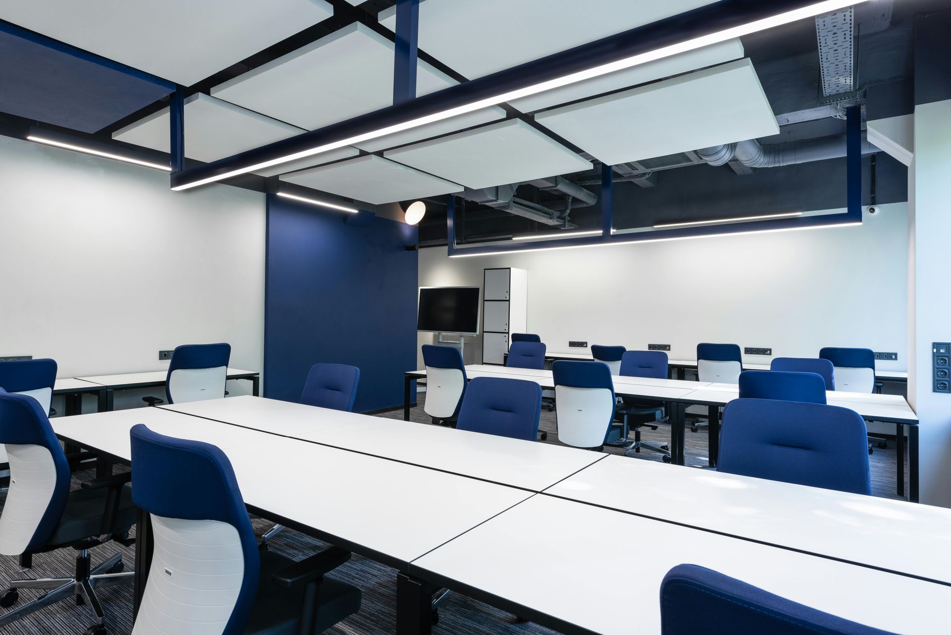 Modern conference room with long white tables, blue chairs, and a dark blue accent wall.
