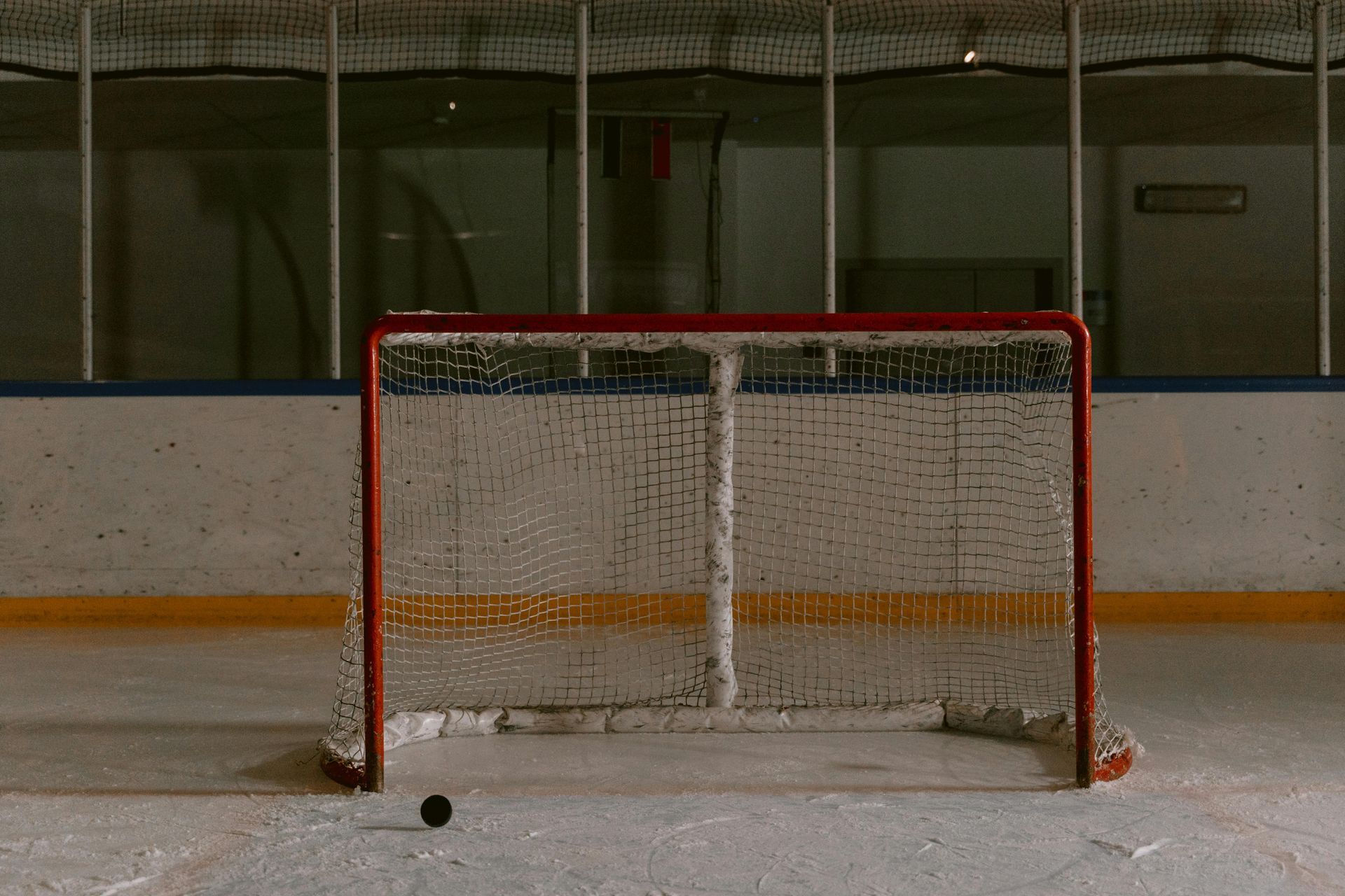Hockey puck in front of an empty hockey net on an ice rink.