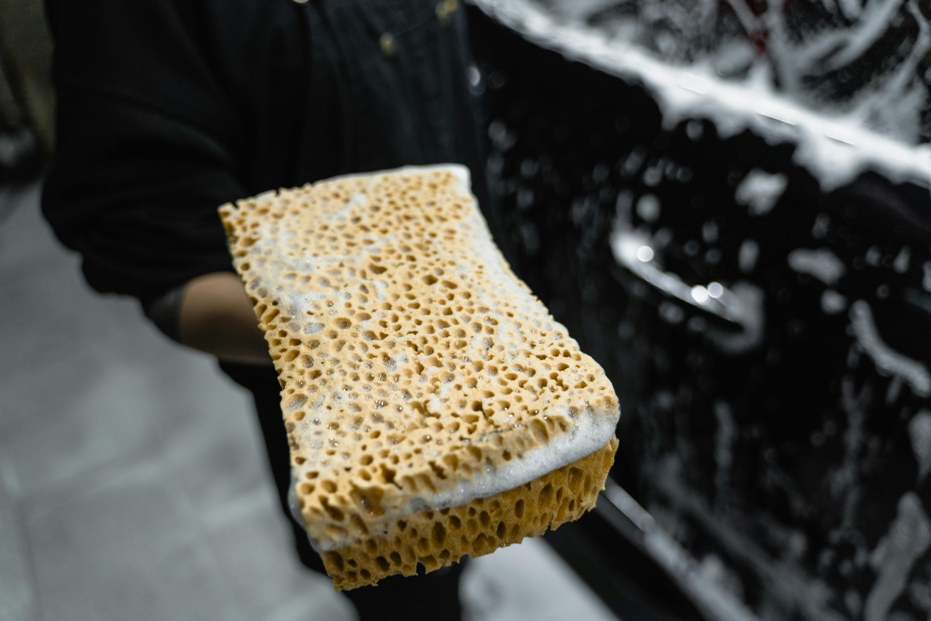 Sponge covered in suds being held next to a soapy car door, about to be used for washing.