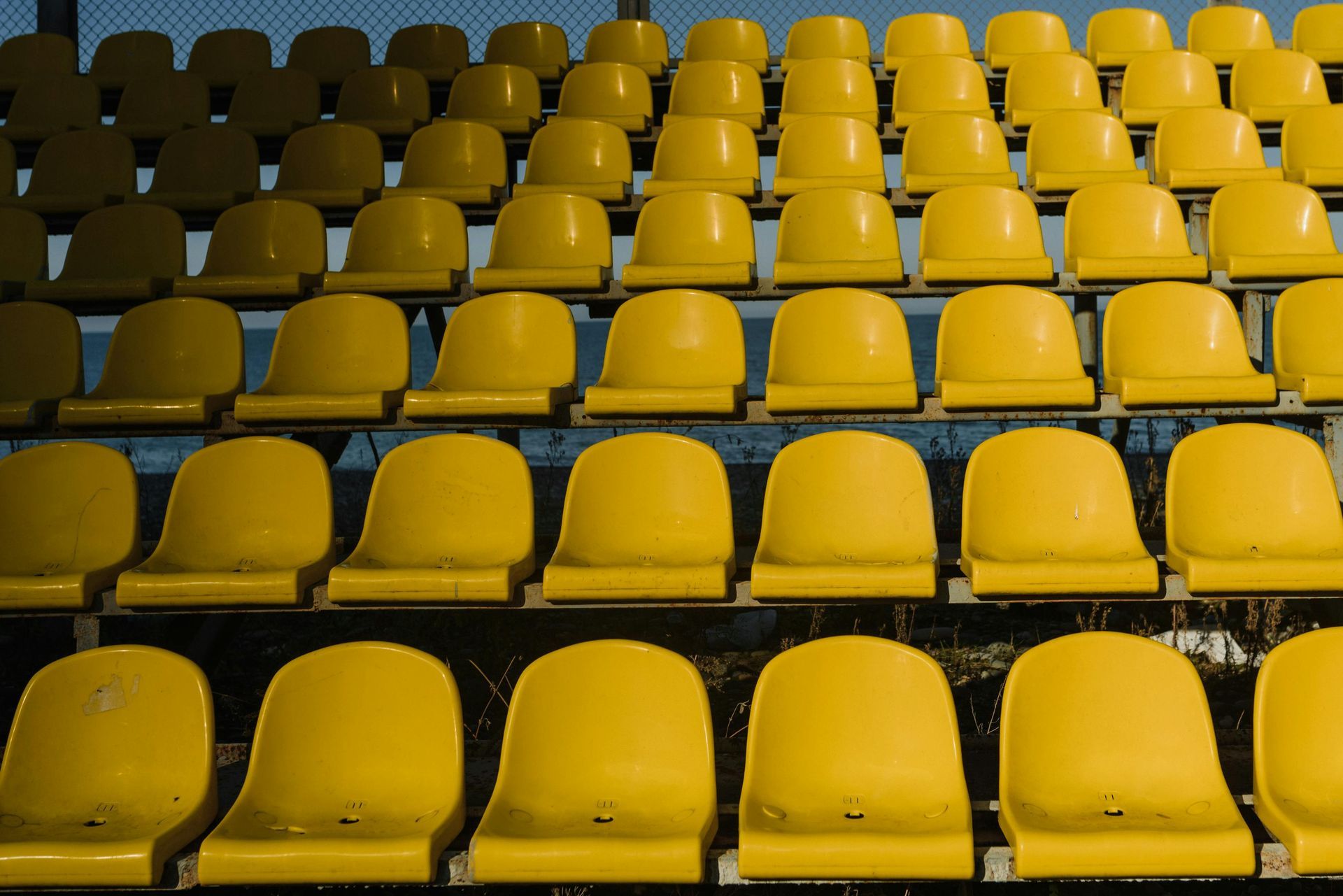 Yellow stadium seats in rows, empty, under a blue net.