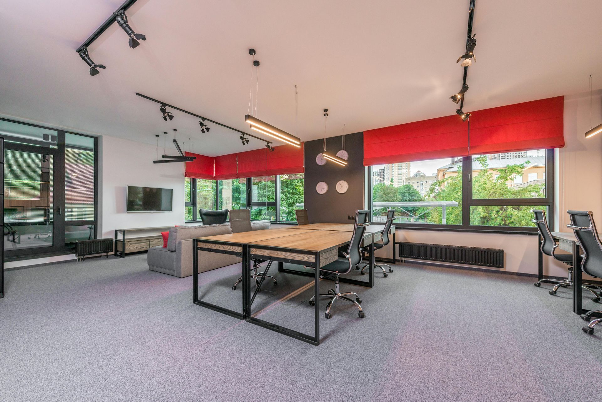 Modern office space with a large table, multiple chairs, red window shades, and large windows.