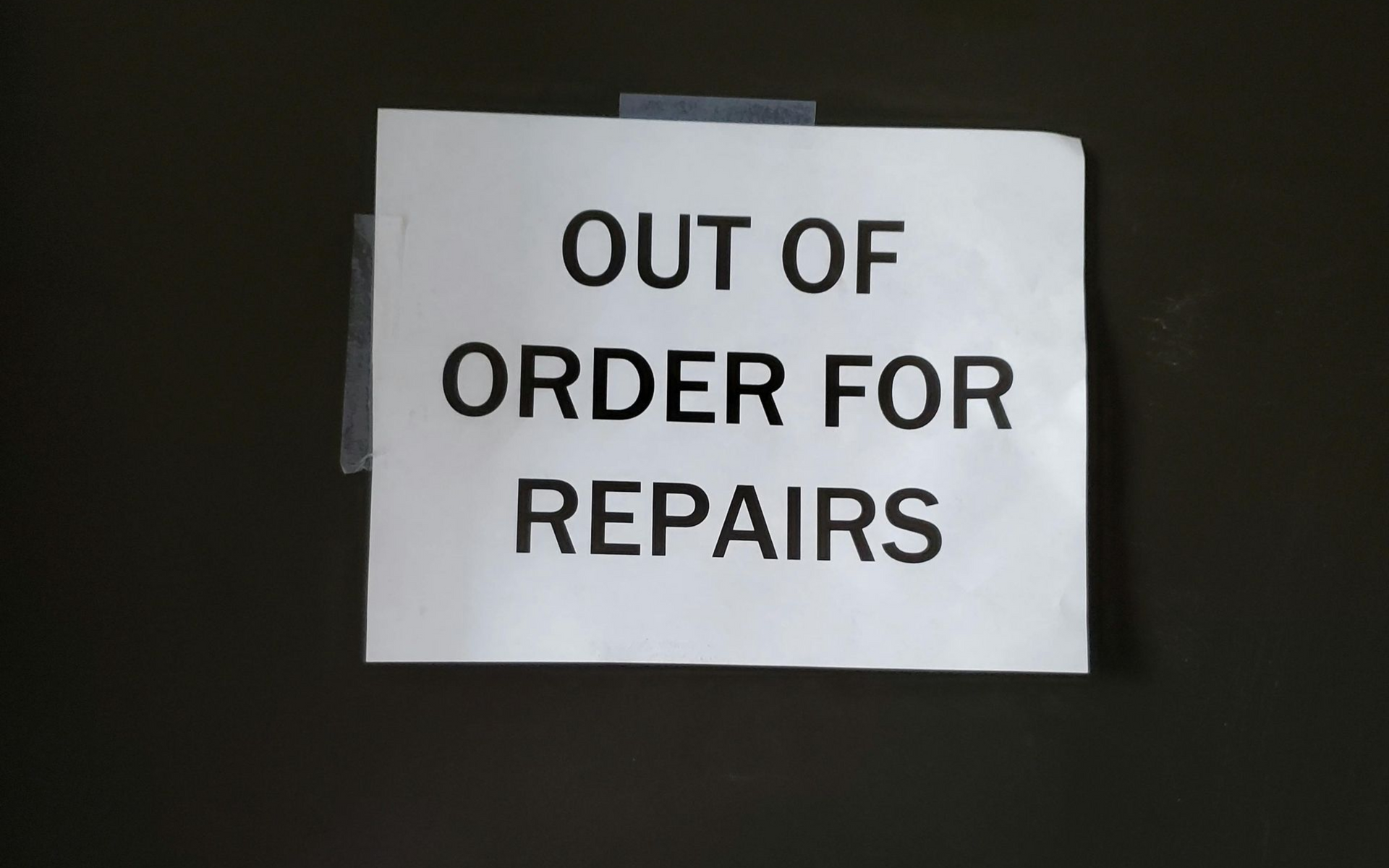 White paper sign taped to a dark surface reads 