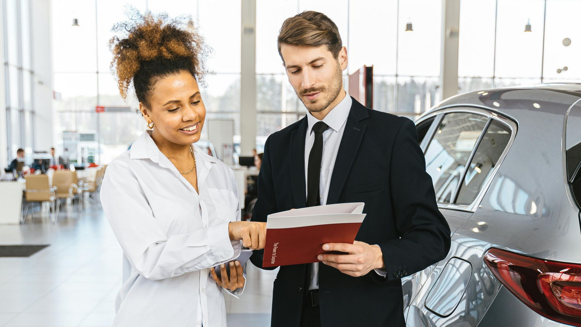 Woman and man reviewing paperwork near a car in a dealership.
