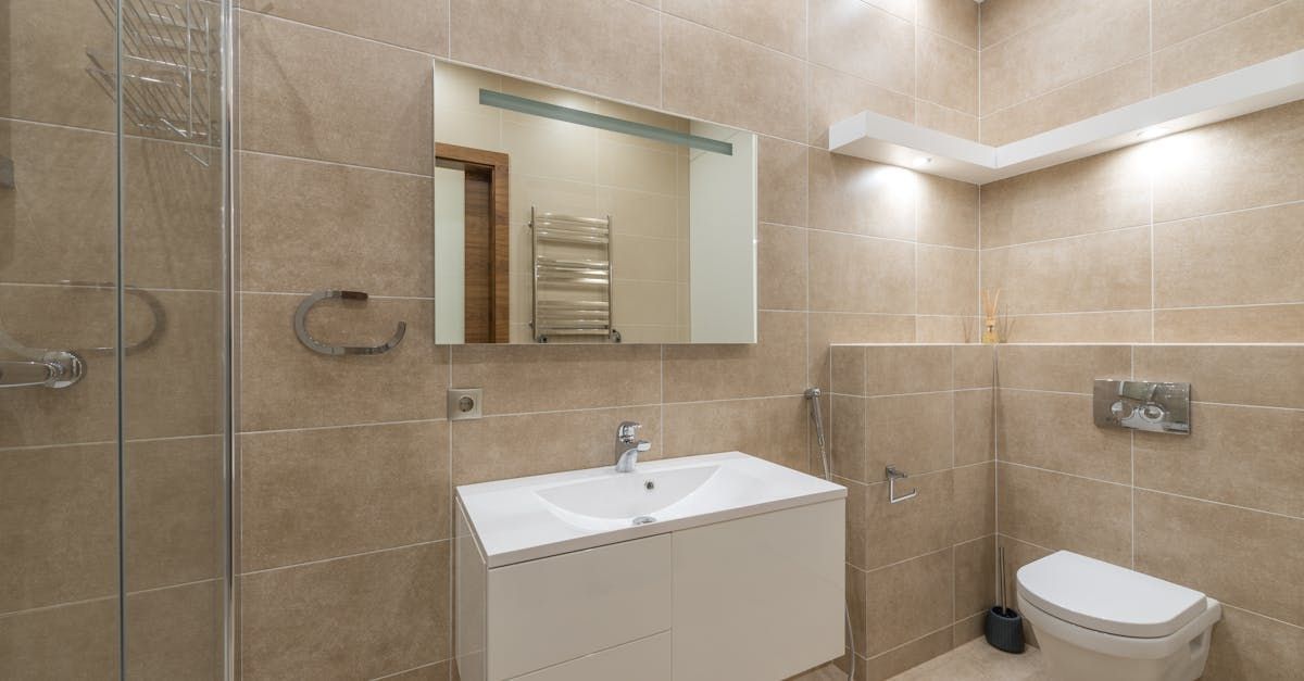 Bathroom with beige tile walls, white sink, toilet, and shower. A mirror is above the sink.