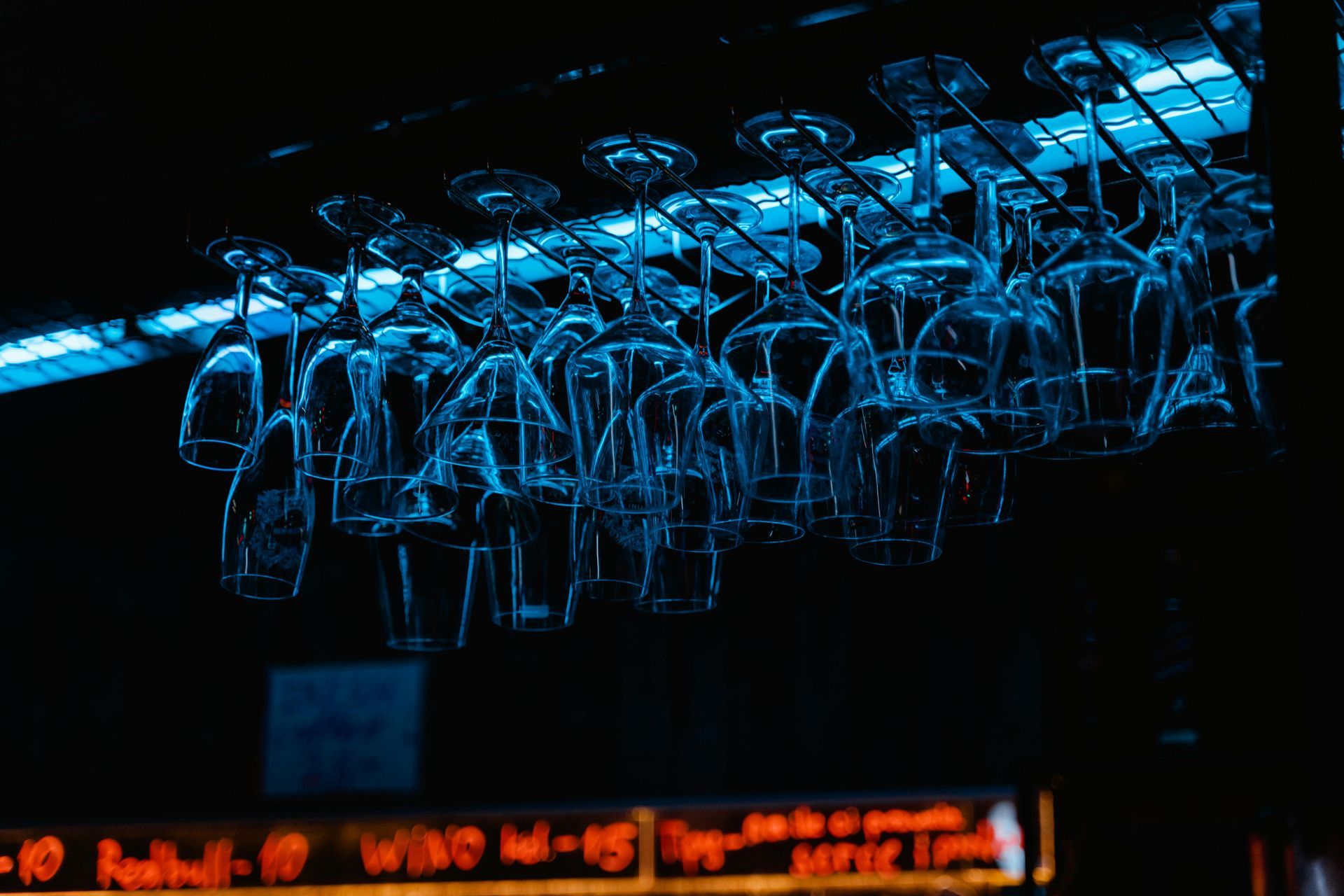 Wine glasses hanging upside down in a bar, illuminated with blue light.