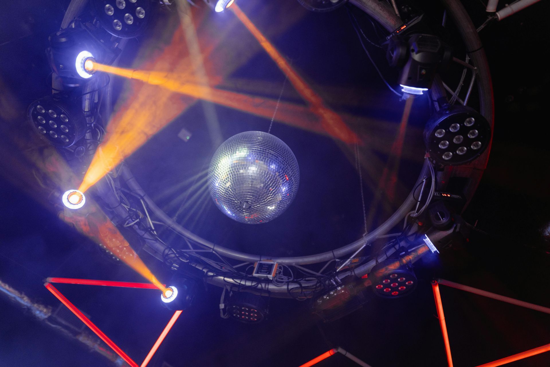 Disco ball hanging, encircled by stage lights, orange and blue beams, in a dark space.