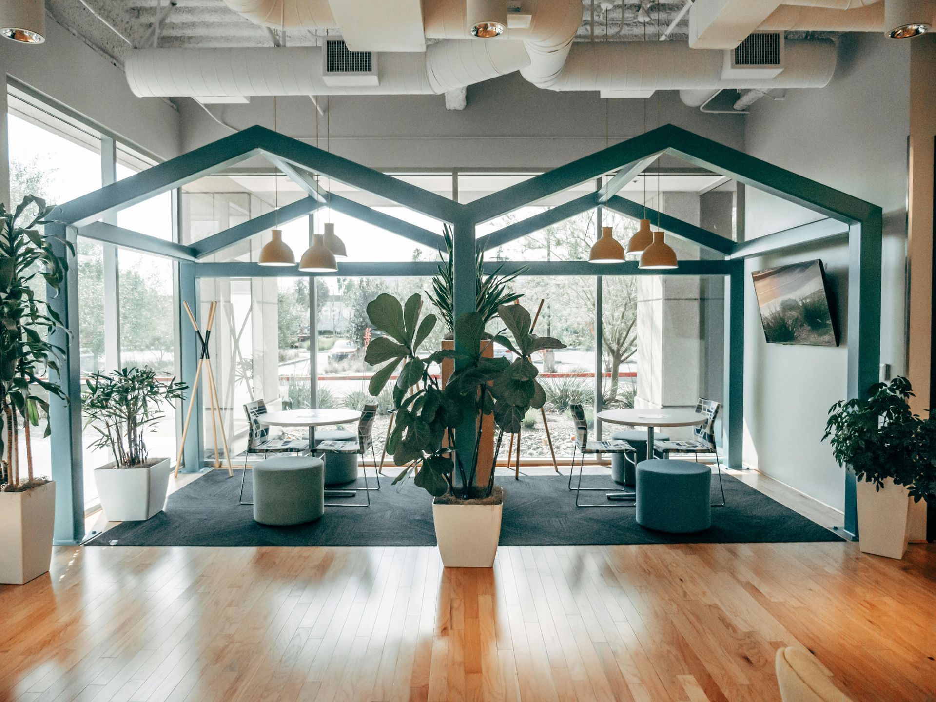 Two teal-framed structures in a room with plants, tables, and round stools, lit by yellow pendant lights.
