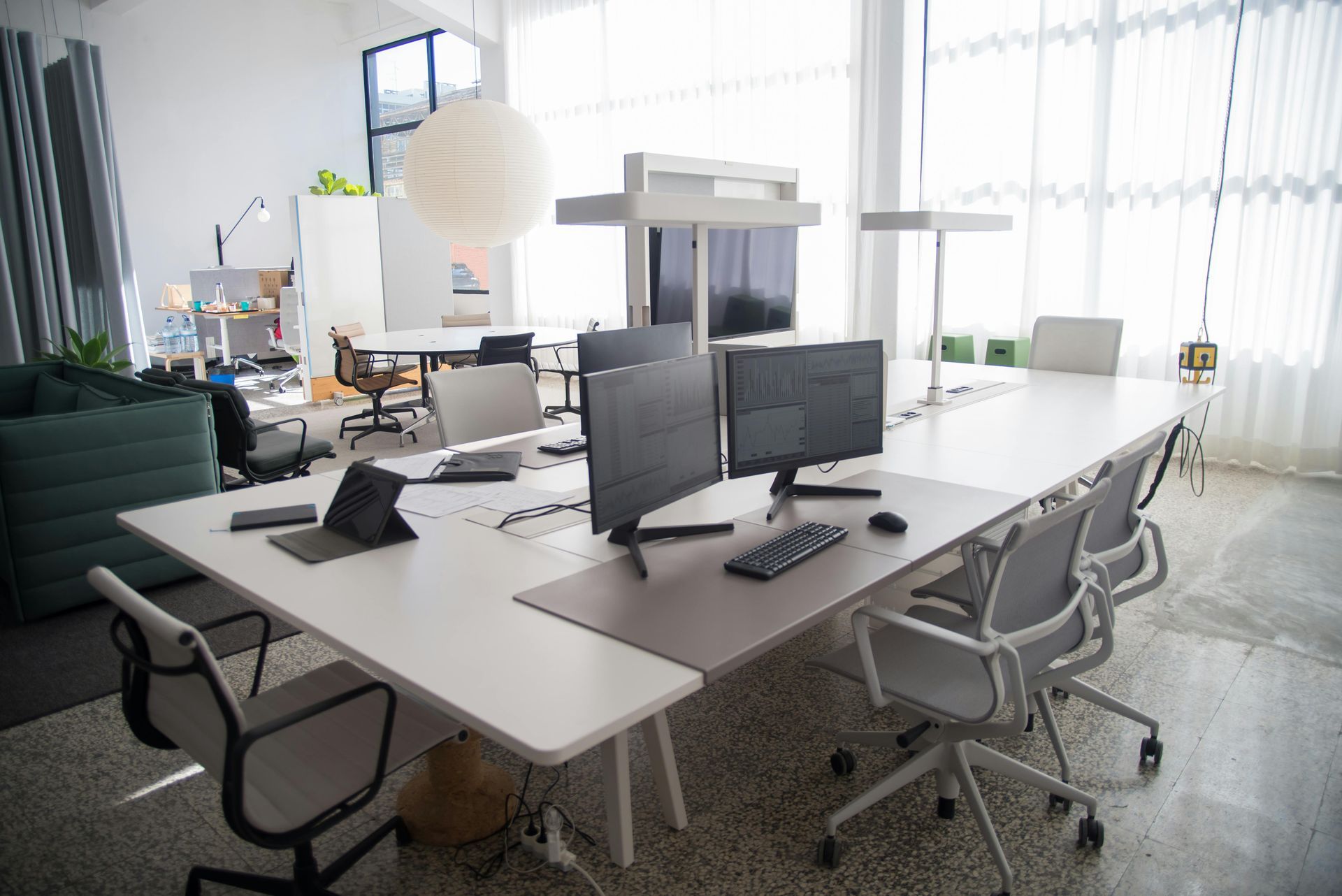 Modern office space with white desks, computers, and gray chairs. Bright natural light.
